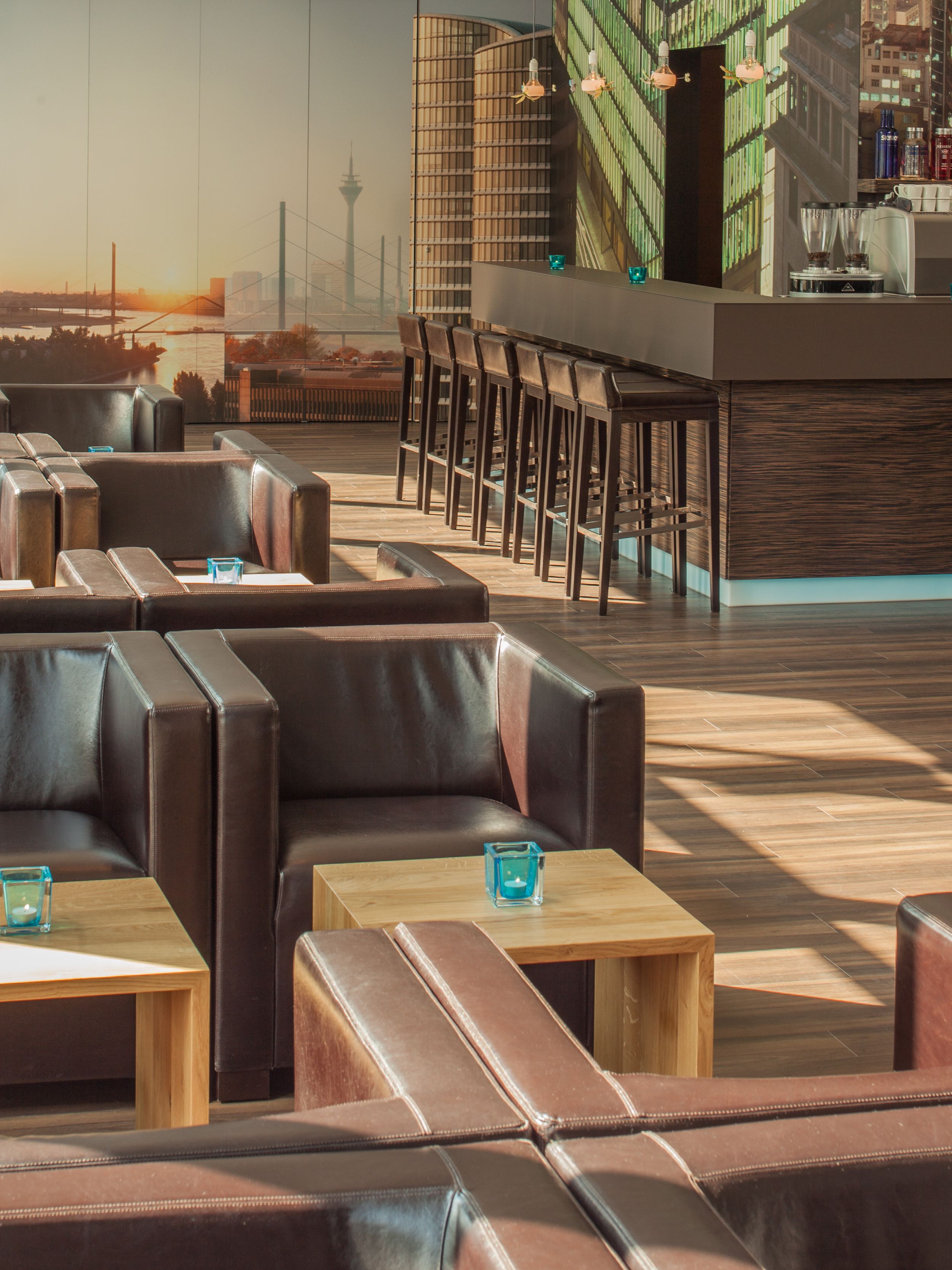 hotel Düsseldorf Hauptbahnhof Motel One lounge with sunlight and several armchairs, as well as the bar in the background