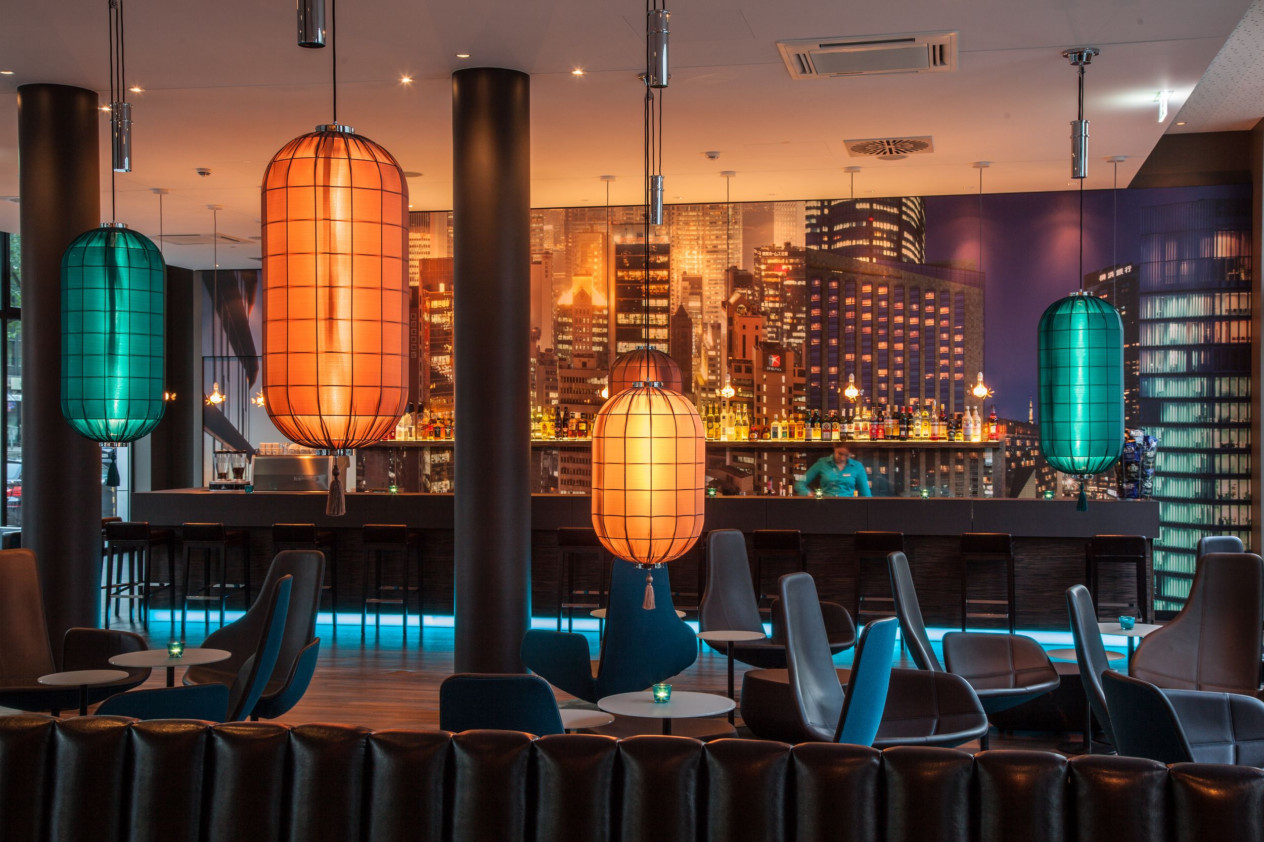 Hotel Düsseldorf Hauptbahnhof Motel One Bar mit Mitarbeiterin bei der Arbeit sowie Sitzgelegenheiten im Vordergrund