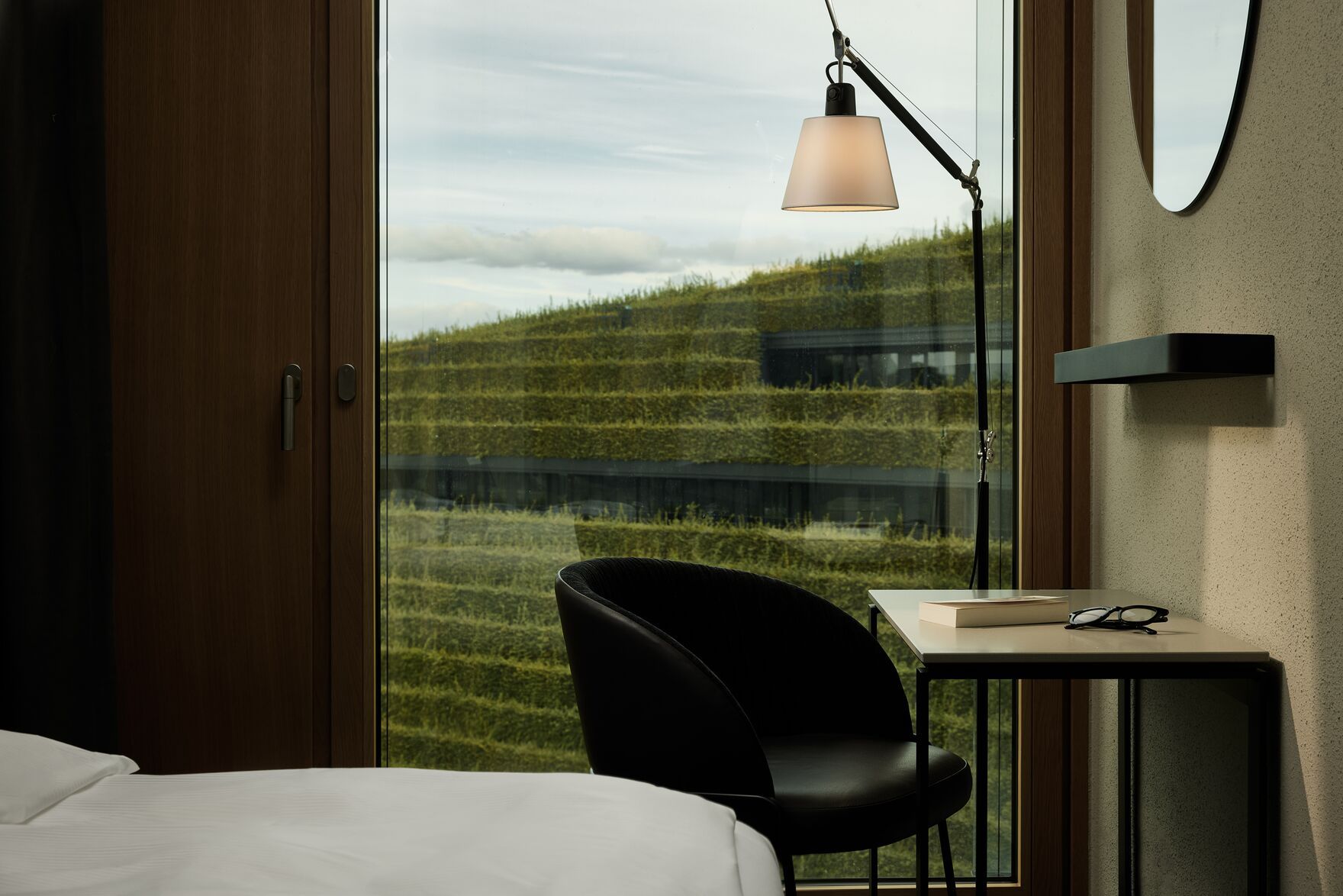 Designhotel Düsseldorf KöBogen The Cloud One Zimmer mit Bett, schwarzem Sessel und Tisch vor bodentiefem Fenster