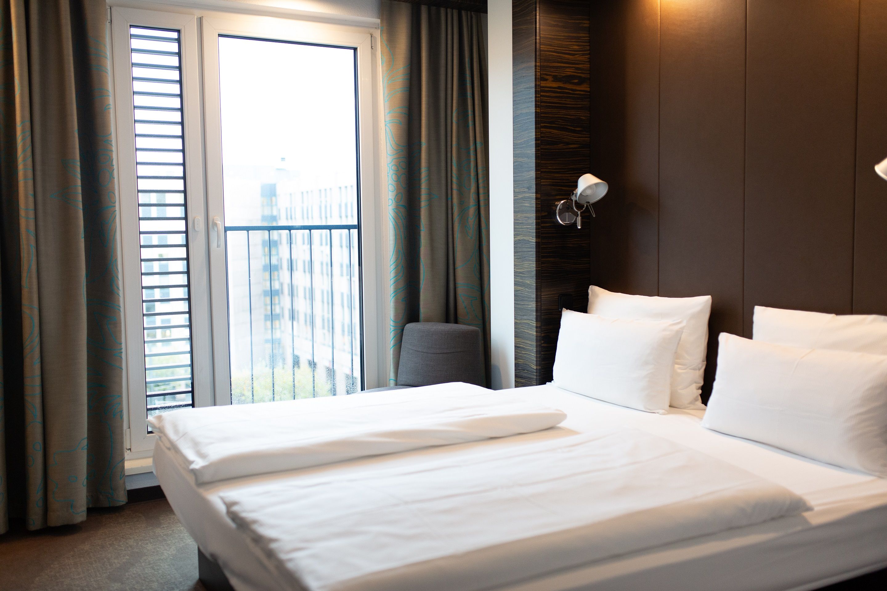 Hotel Düsseldorf Hauptbahnhof Motel One seitlicher Blick in helles Zimmer mit großem Doppelbett und bodentiefem Fenster