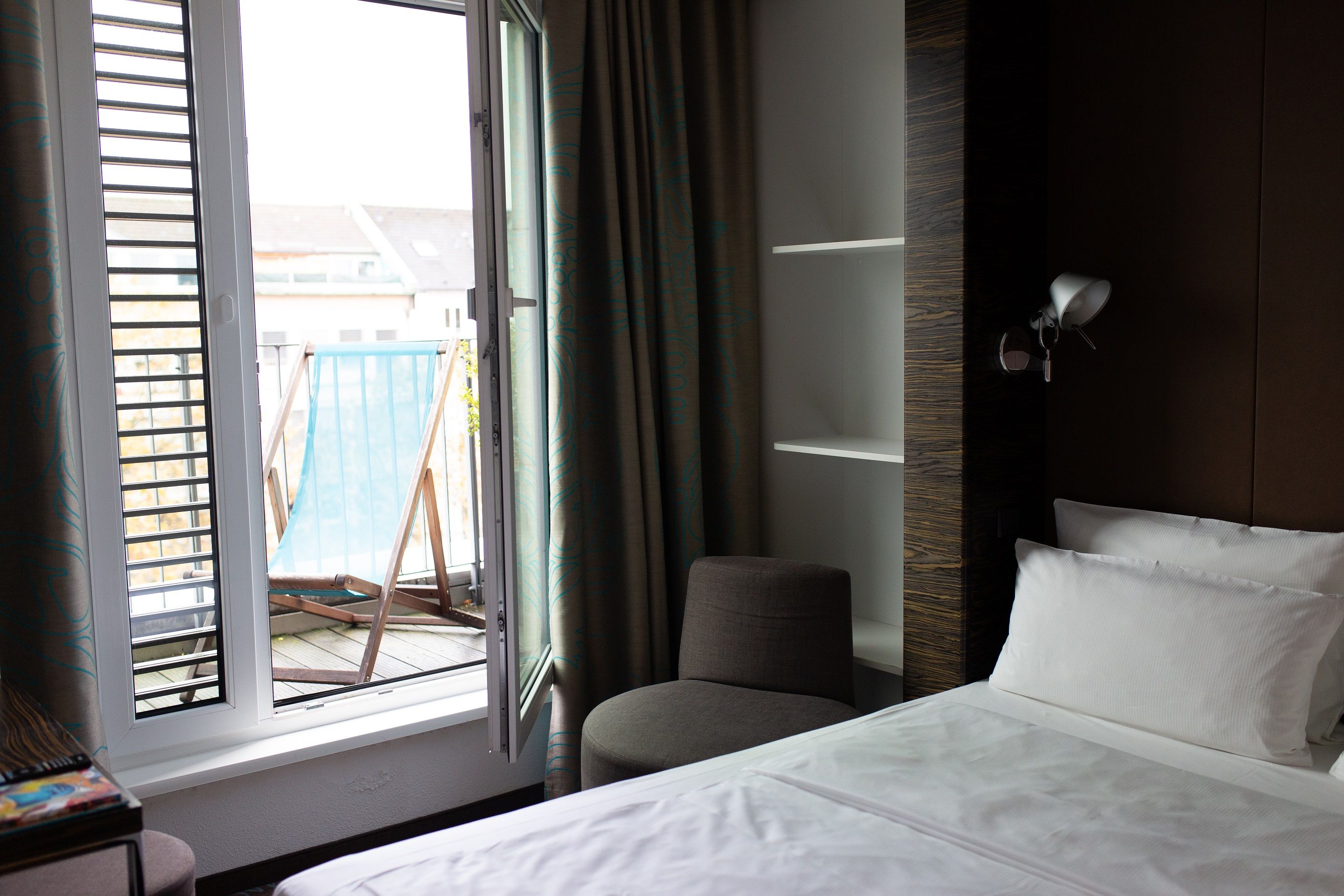 Hotel Düsseldorf Hauptbahnhof Motel One Balkonzimmer mit Bett und offener Tür zum Balkon, auf dem ein Liegestuhl steht