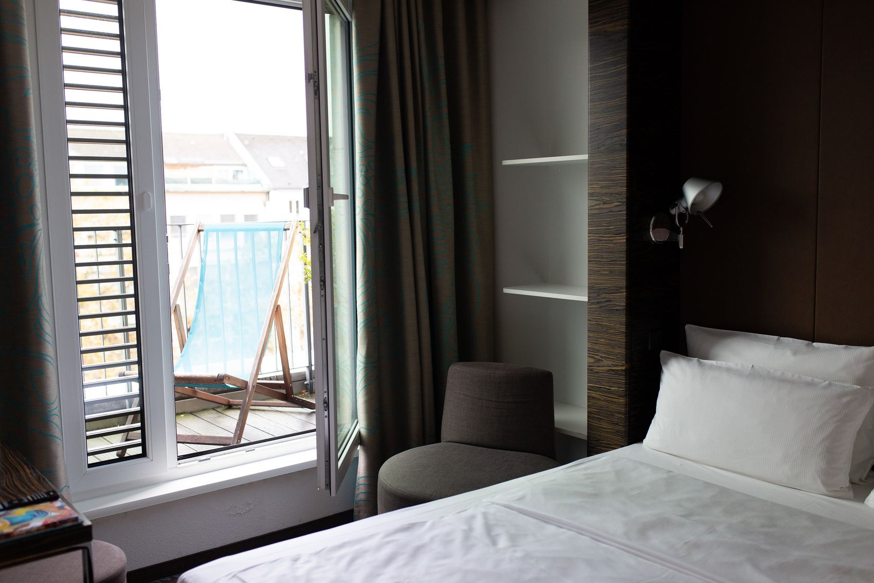 Hotel Düsseldorf Hauptbahnhof Motel One Balkonzimmer mit Bett und offener Tür zum Balkon, auf dem ein Liegestuhl steht