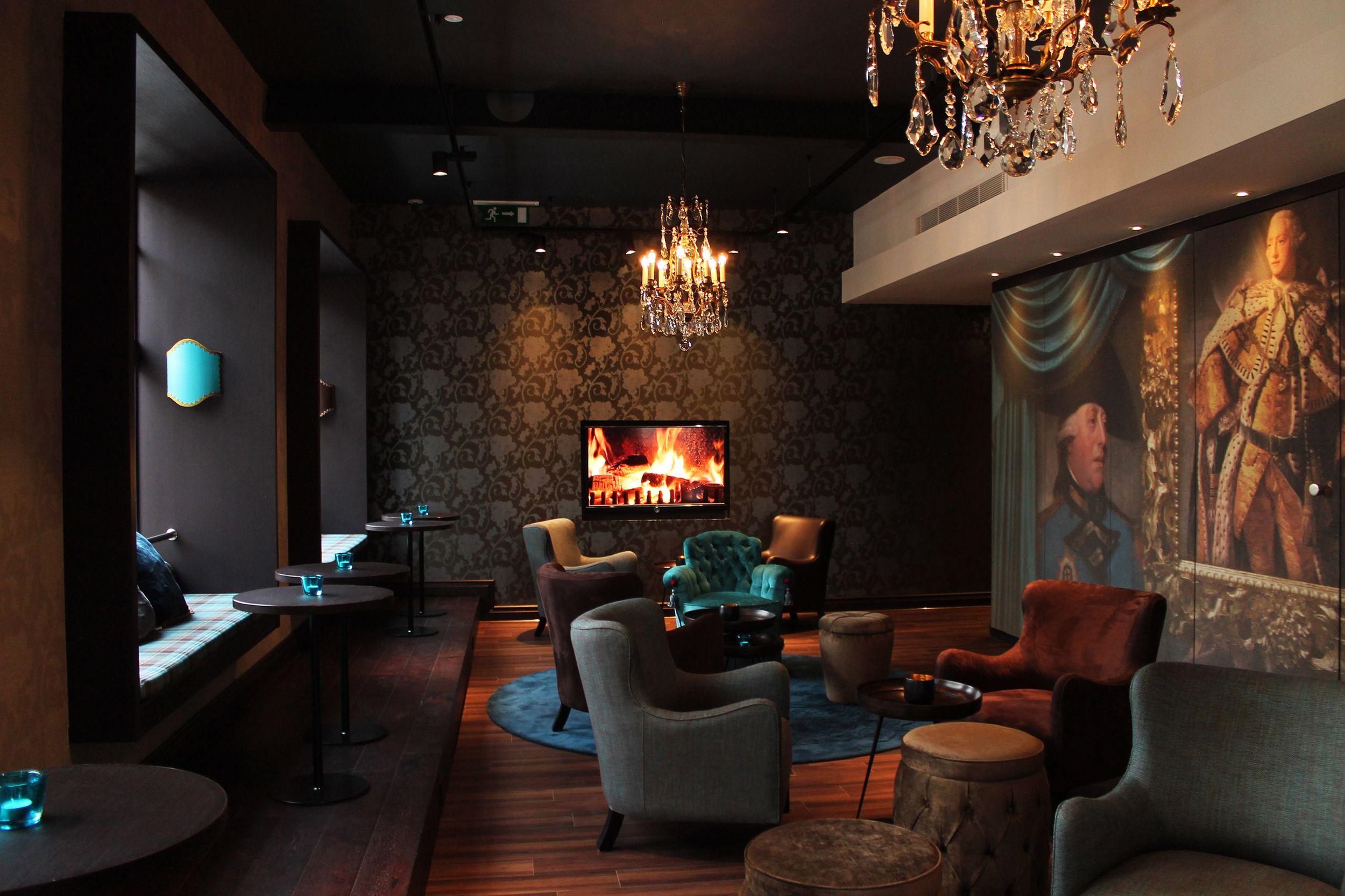 Hotel Edinburgh Princes Motel One Lounge mit Sesseln und Tischen sowie einem Fernseher mit Feuermotiv an der Wand