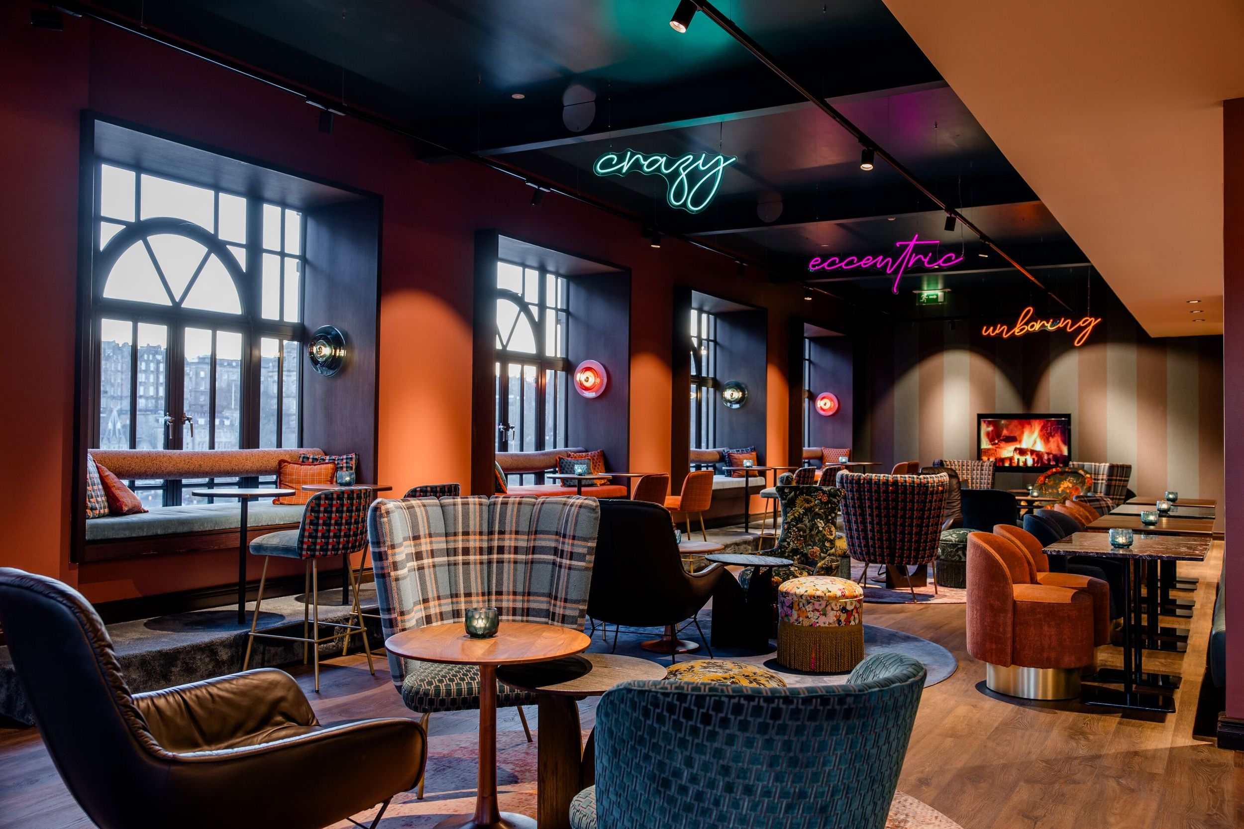 Hotel Edinburgh Princes Motel One große Lounge mit mehreren Sitzgelegenheiten sowie drei Neonschilder in unterschiedlichen Farben, die von der Decke hängen