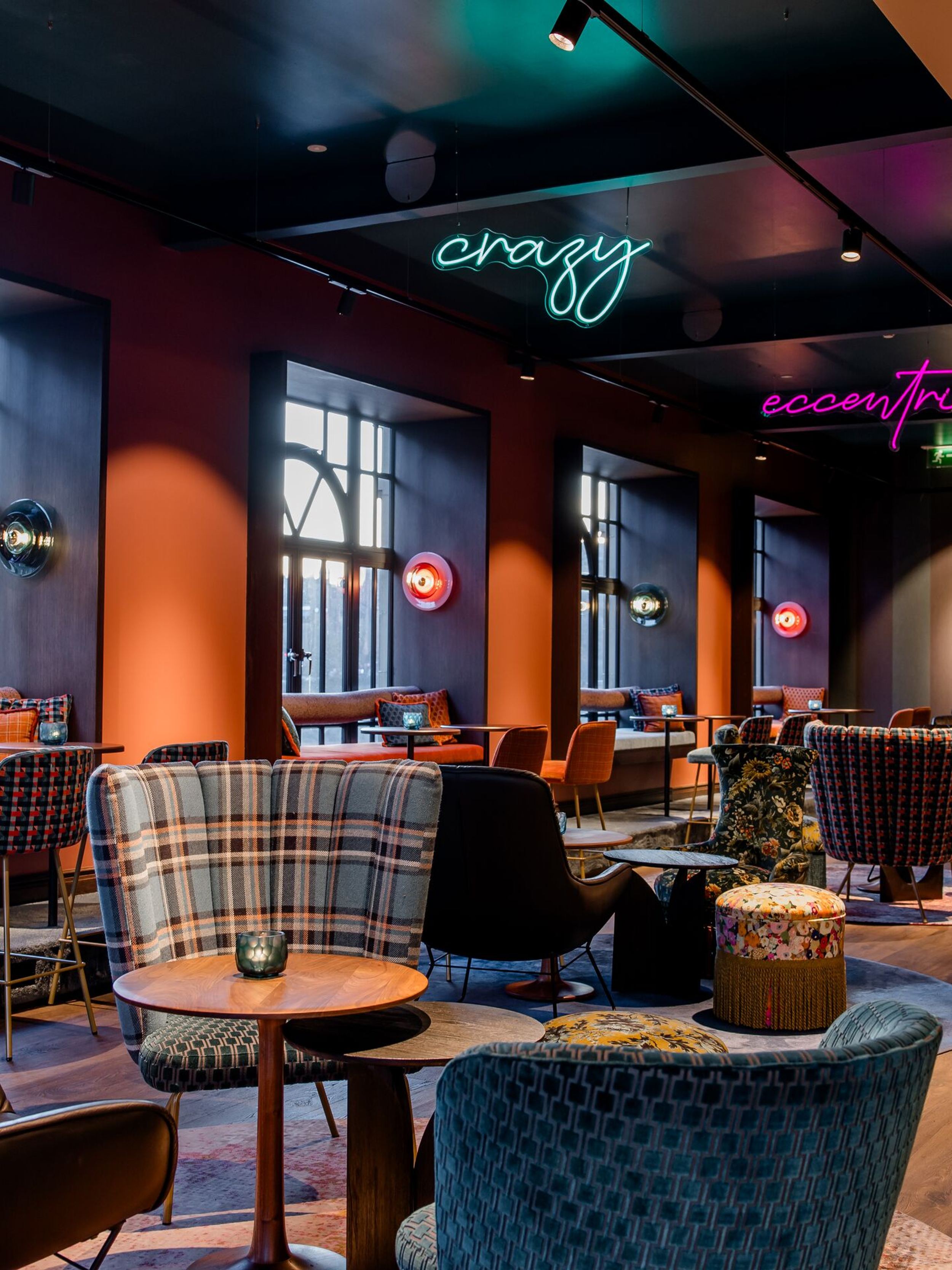 Hotel Edinburgh Princes Motel One große Lounge mit mehreren Sitzgelegenheiten sowie drei Neonschilder in unterschiedlichen Farben, die von der Decke hängen