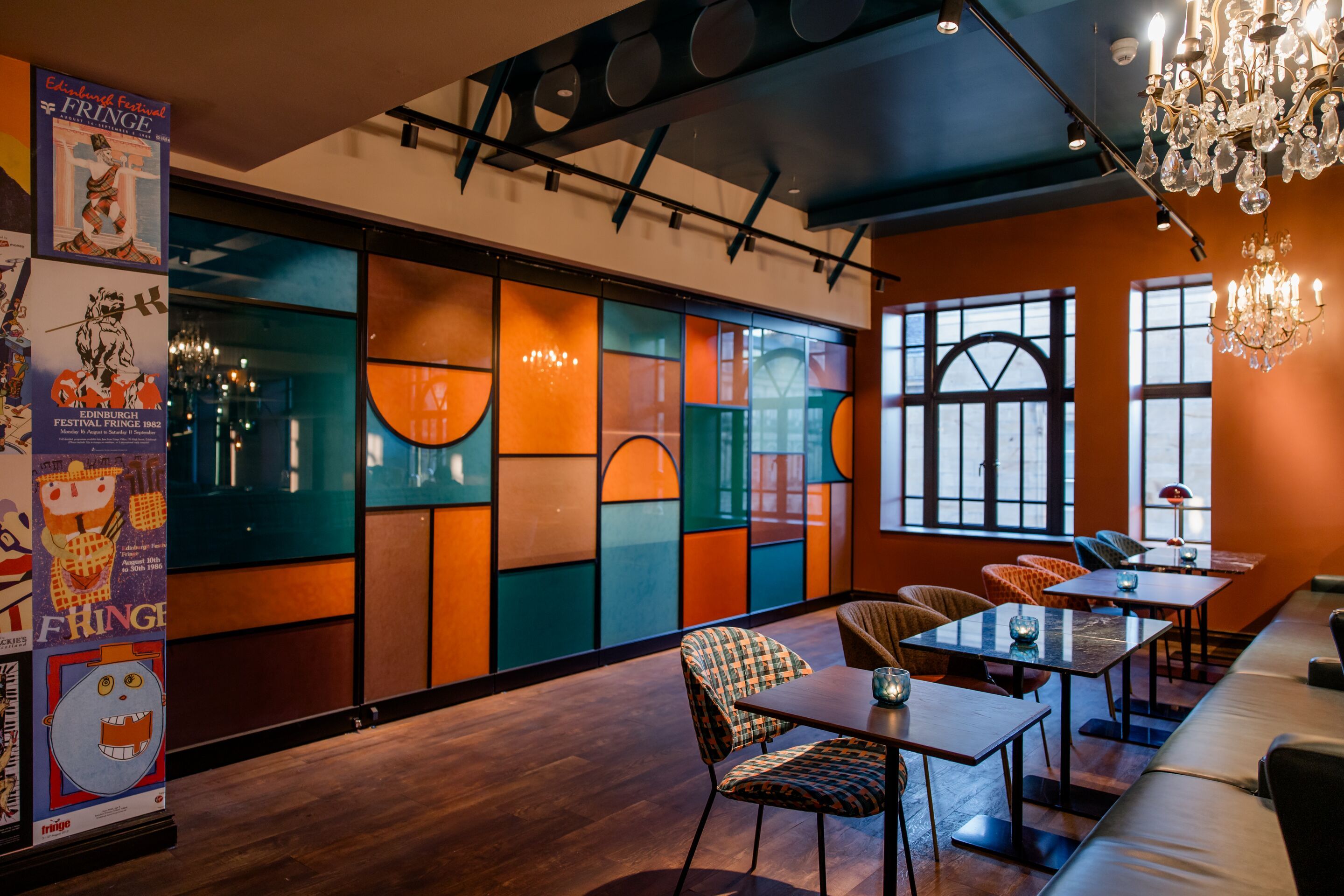 Hotel Edinburgh Princes Motel One Blick auf mehrere Tische und Stühle sowie eine große Glaswand in den Farben türkis, orange und braun