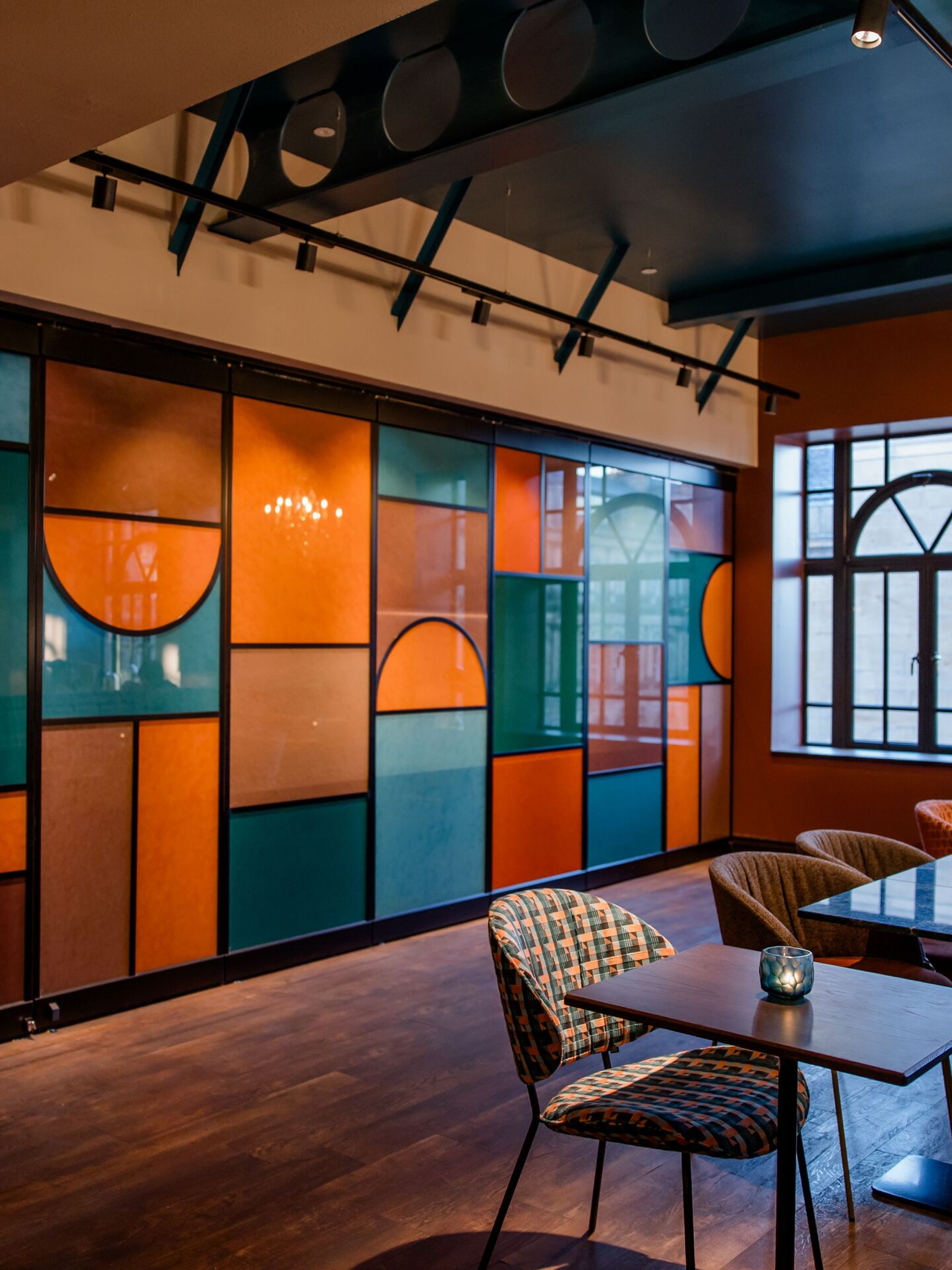 Hotel Edinburgh Princes Motel One Blick auf mehrere Tische und Stühle sowie eine große Glaswand in den Farben türkis, orange und braun