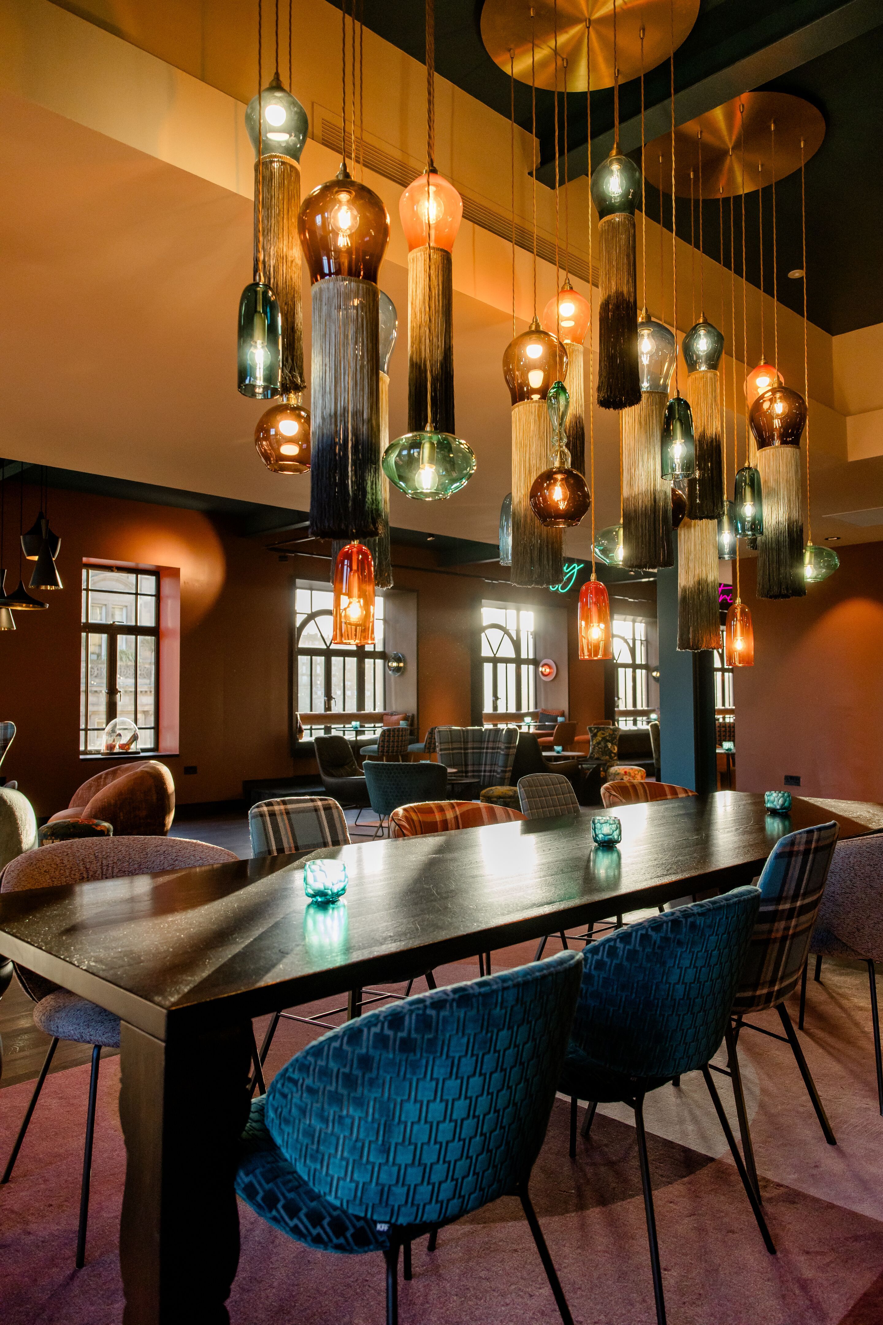 Hotel Edinburgh Princes Motel One offene Lounge mit Blick über einen großen Tisch und Deckenlampen auf mehrere Sitzgelegenheiten 