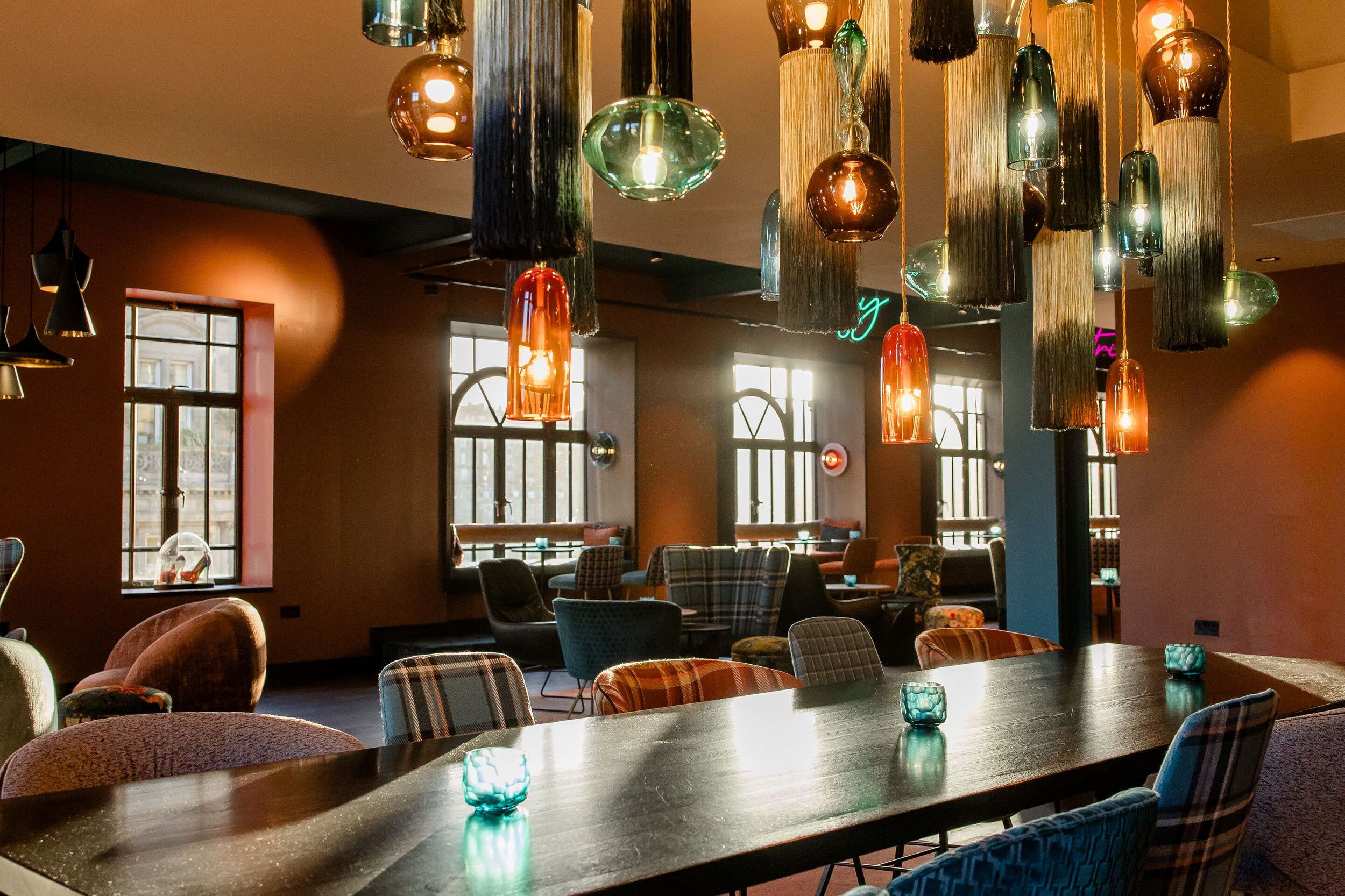 Hotel Edinburgh Princes Motel One offene Lounge mit Blick über einen großen Tisch und Deckenlampen auf mehrere Sitzgelegenheiten