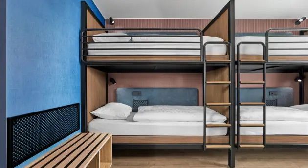 Zweckmäßig eingerichtetes Zimmer mit Etagenbetten, kombiniert aus Holz und Metall, mit moderner Beleuchtung und schlichtem, freundlichem Design, ideal für Gruppenreisende oder Familien.
