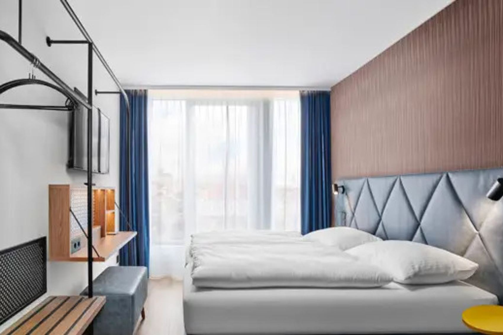 Hotel Erfurt-City Modernes Hotelzimmer mit großem Bett, weichen Kopfkissen, Fenster mit blickdichten Vorhängen und Tageslicht. Helle, freundliche Atmosphäre mit elegantem Holz- und Stoffdesign. Schreibtisch und praktische Ablagen für Reisende.