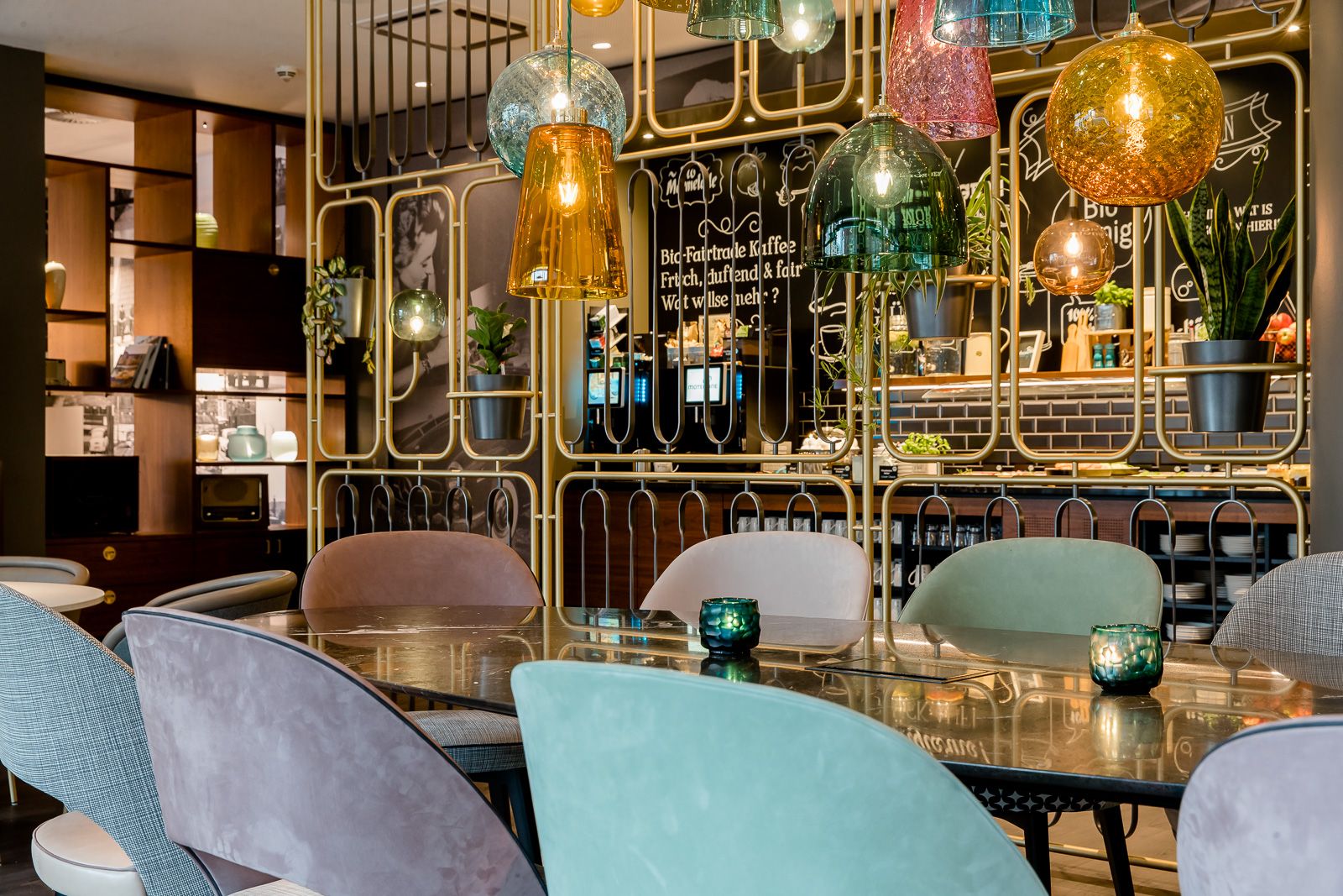 Hotel Essen Motel One lichtdurchflutete Lounge mit Blick auf einen großen Tisch sowie dem Frühstücksbuffet im Hintergrund