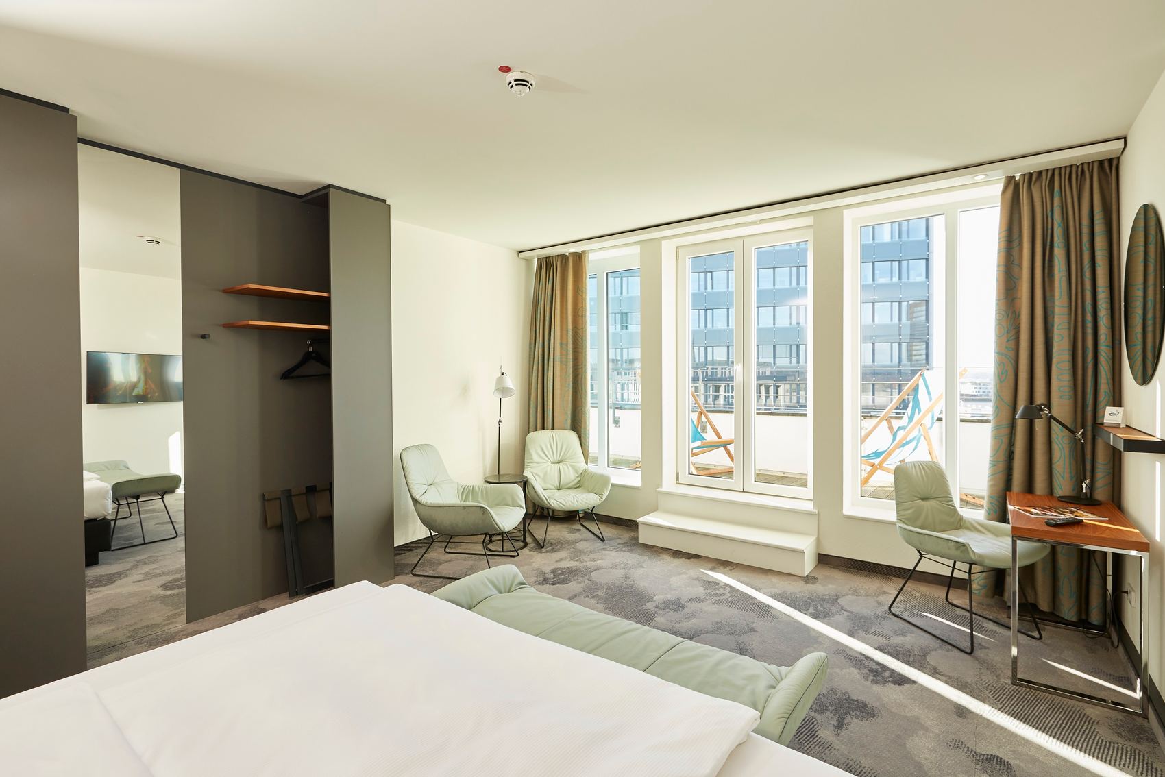 Hotel Essen Motel One lichtdurchflutetes Zimmer mit Bett, drei Sesseln sowie Balkonzugang mit zwei Liegestühlen