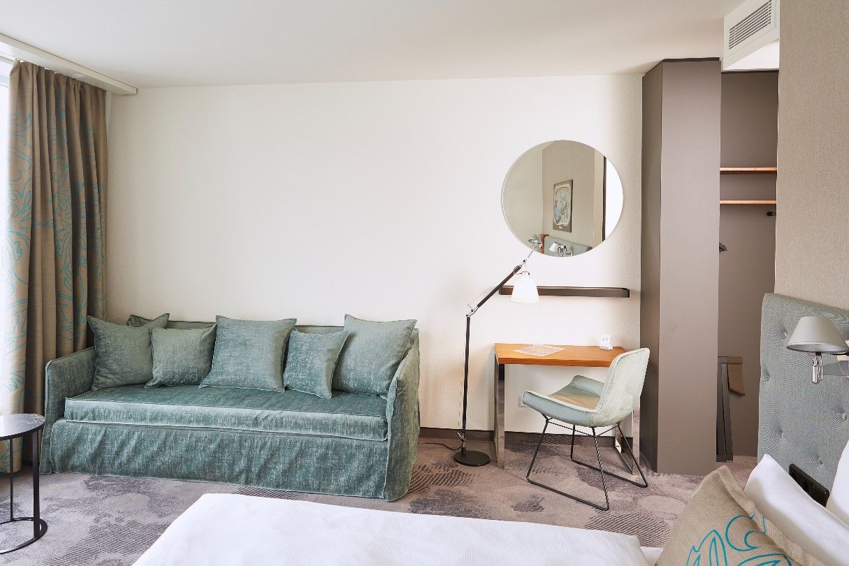 Hotel Essen Motel One helles Zimmer mit Blick auf eine große Couch, Bett, Schreibtisch und Stuhl