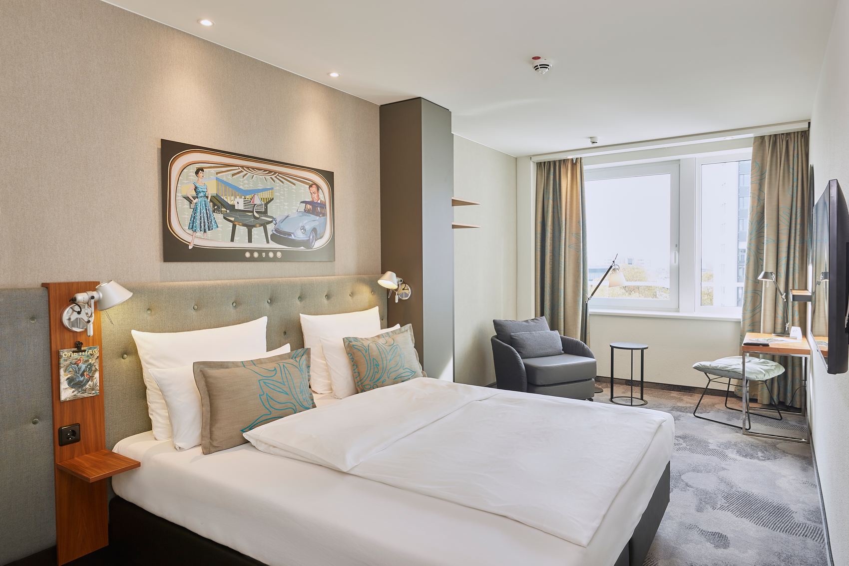 Designhotel Essen Motel One lichtdurchflutetes Zimmer mit geräumigem Doppelbett, Sessel, Schreibtisch und Fernseher an der Wand