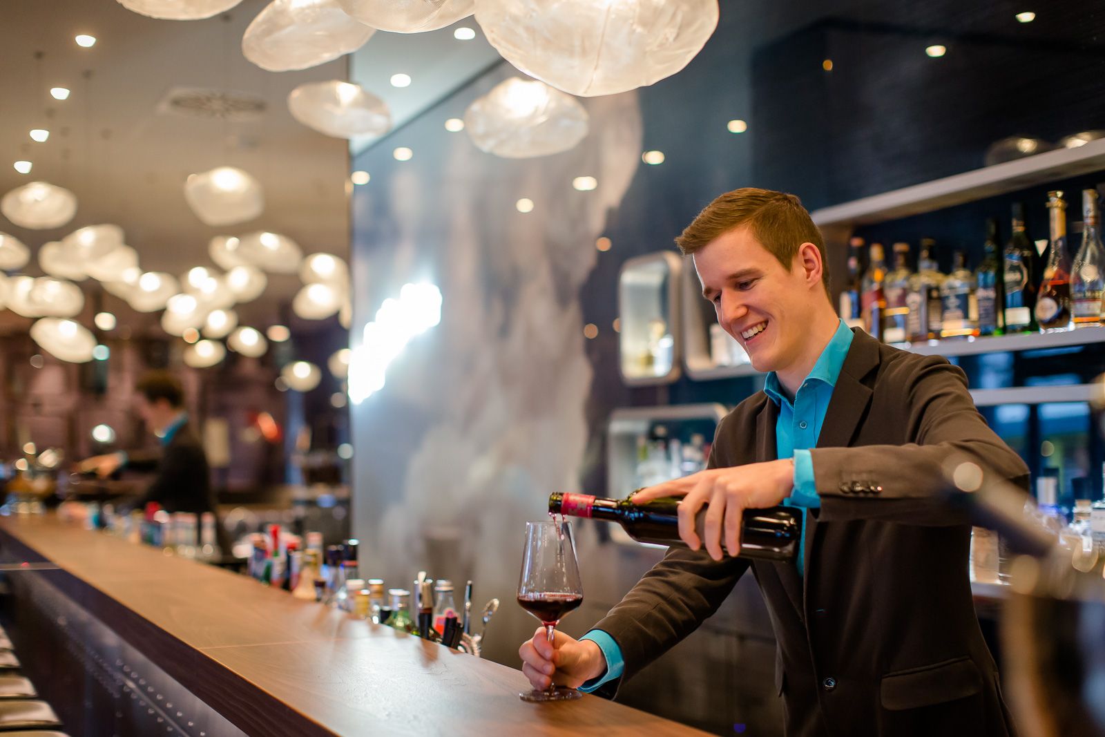 Hotel Frankfurt Airport Motel One lächelnder Barkeeper an der Bar füllt ein Glas Rotwein ein