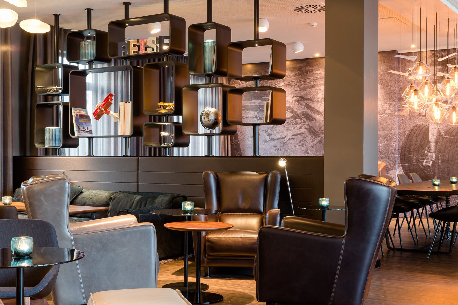 Hotel Frankfurt Airport Motel One offene Lounge mit mehreren Sitzgelegenheiten und großem offenen Regal als Raumtrenner