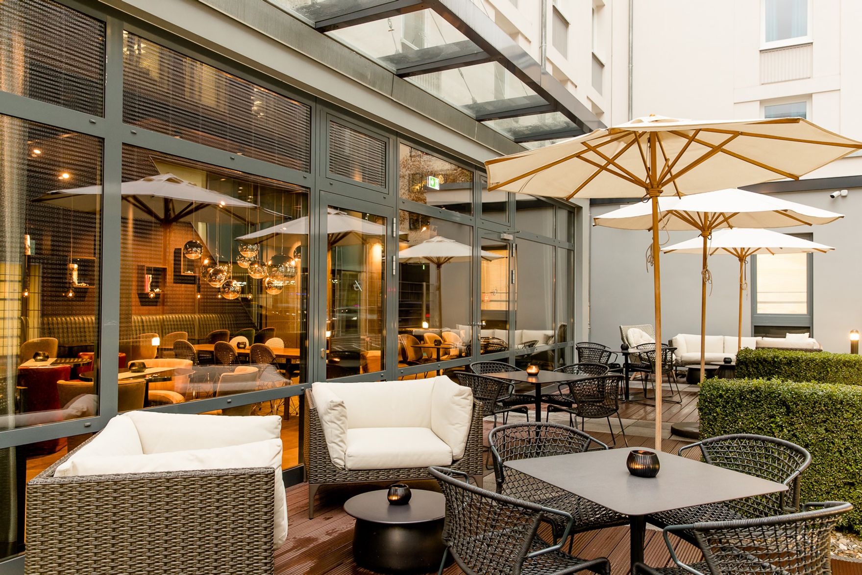 Hotel Frankfurt East Side Motel One große Terrasse mit mehreren Sitzgelegenheiten und drei offenen Sonnenschirmen