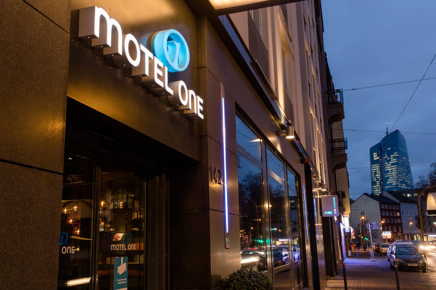 Hotel Frankfurt East Side Motel One Blick von außen bei Abend auf den Eingangsbereich des Hotels mit Logo