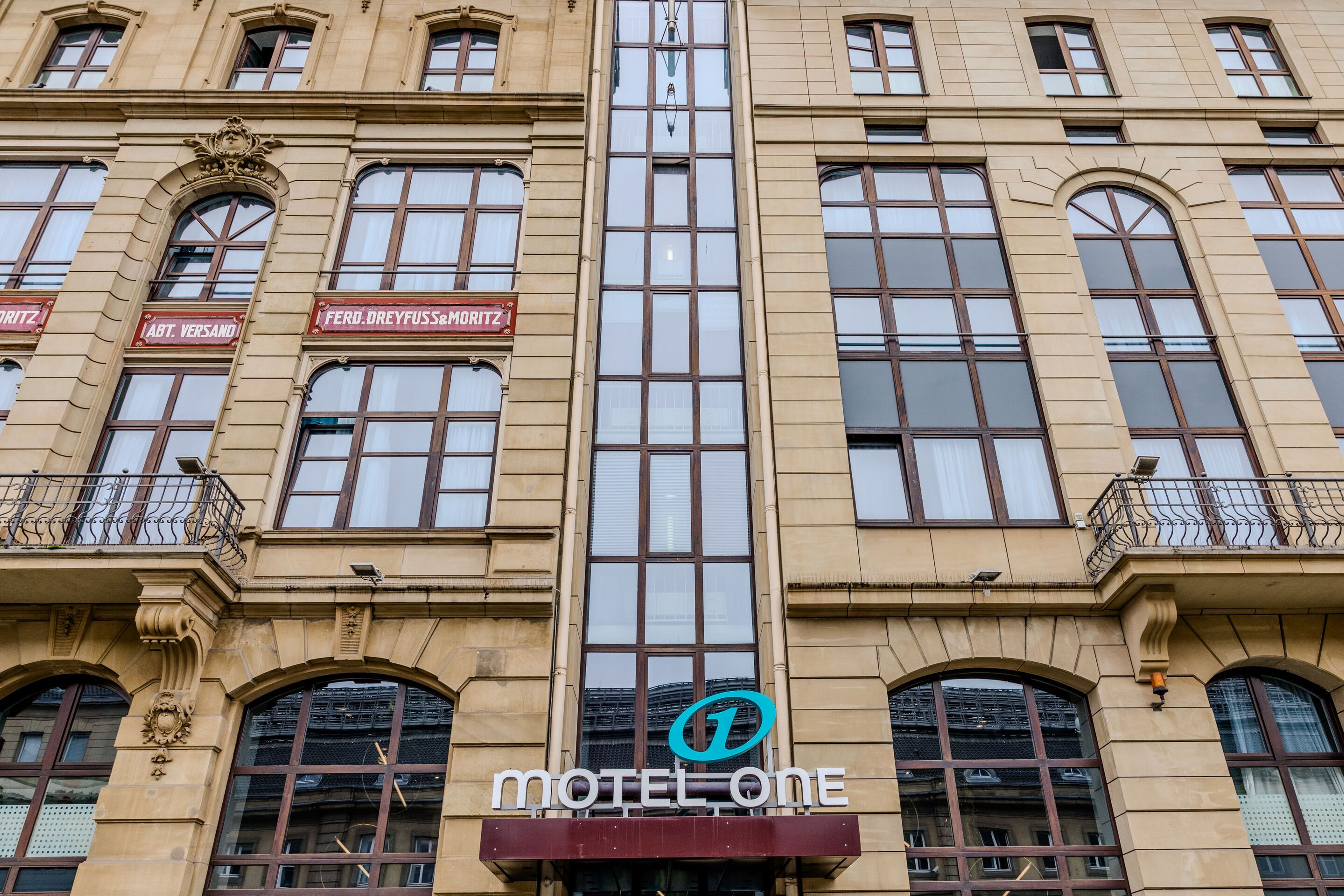 Hotel Frankfurt Hauptbahnhof Motel One Fassade eines Gebäudes mit großen Fenstern, in dessen Mitte ein moderner gläserner Aufzug eingebaut ist, darunter ist das Logo und Schriftzug „Motel One“ zu sehen. Hotel Frankfurt Hauptbahnhof Motel One Fassade eines Gebäudes mit großen Fenstern, in dessen Mitte ein moderner gläserner Aufzug eingebaut ist, darunter ist das Logo und Schriftzug „Motel One“ zu sehen.