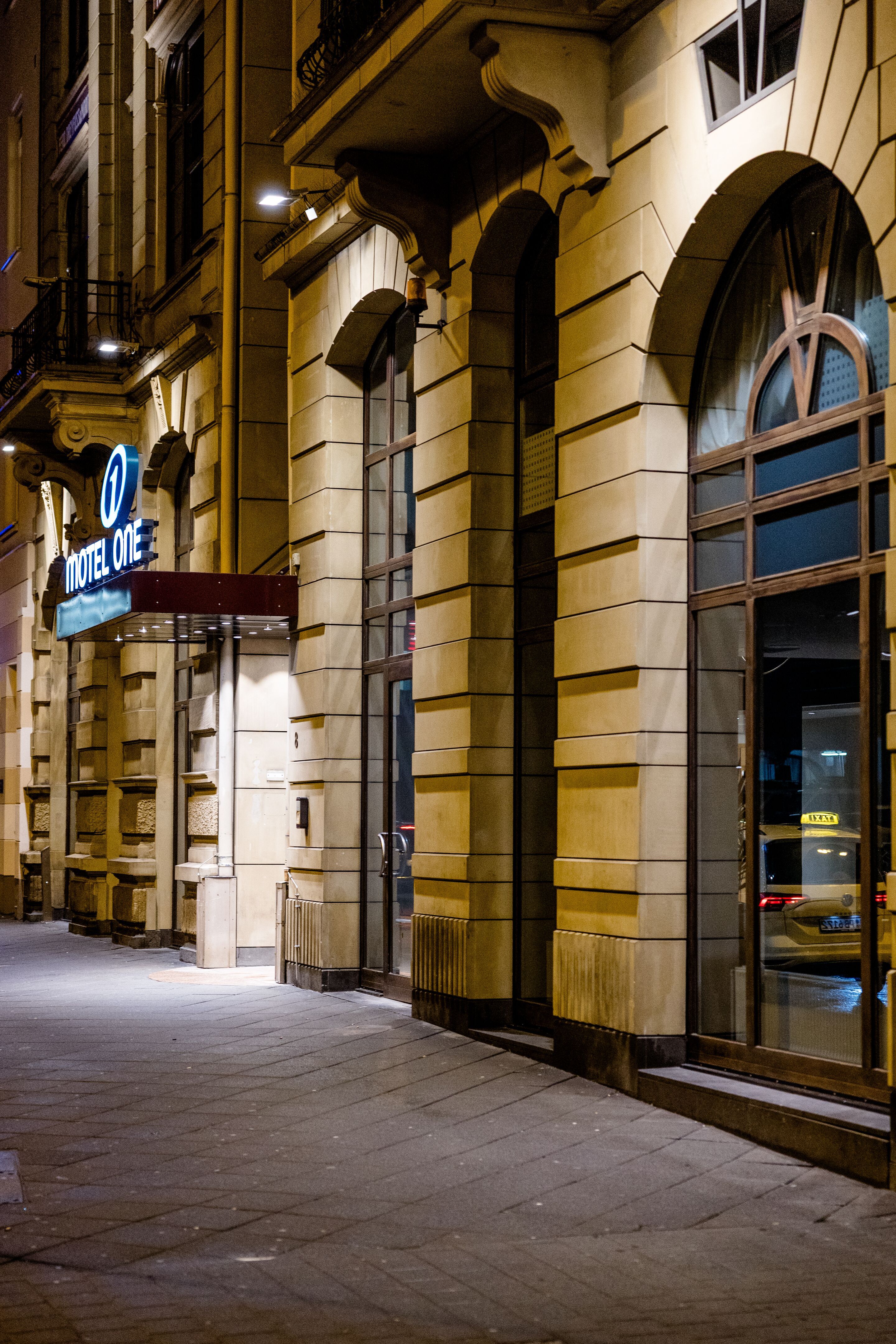 Hotel Frankfurt Hauptbahnhof Motel One Eingang mit Sandsteinfassade und großem Fenster, aufgenommen in der Abenddämmerung, vermittelt einladende Atmosphäre für Reisende.