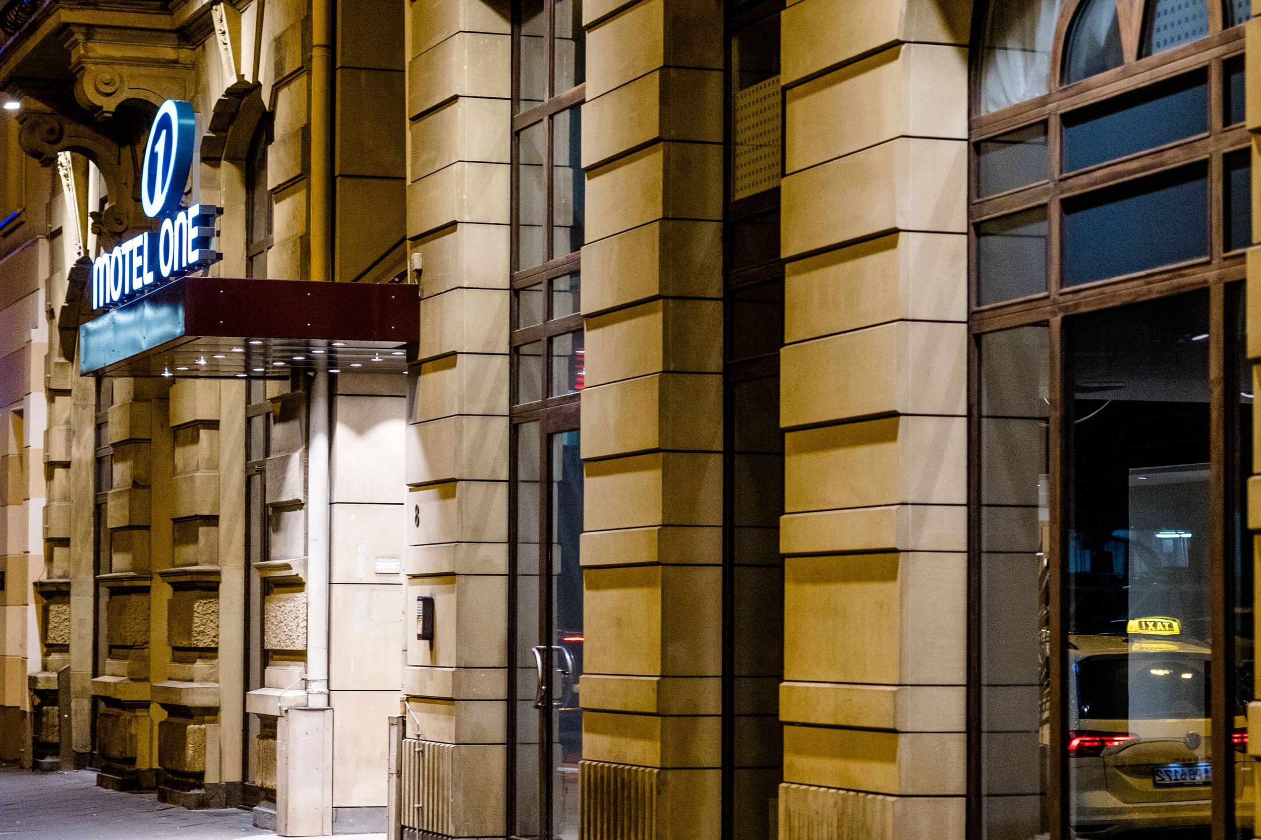 Hotel Frankfurt Hauptbahnhof Motel One Eingang mit Sandsteinfassade und großem Fenster, aufgenommen in der Abenddämmerung, vermittelt einladende Atmosphäre für Reisende.