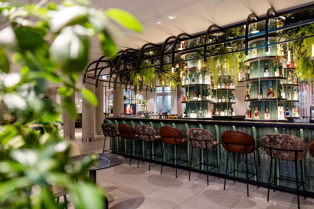 Design hotel Frankfurt-Hauptbahnhof Motel One bar with bar stools, green plant decorations and stylishly arranged drinks bottles.