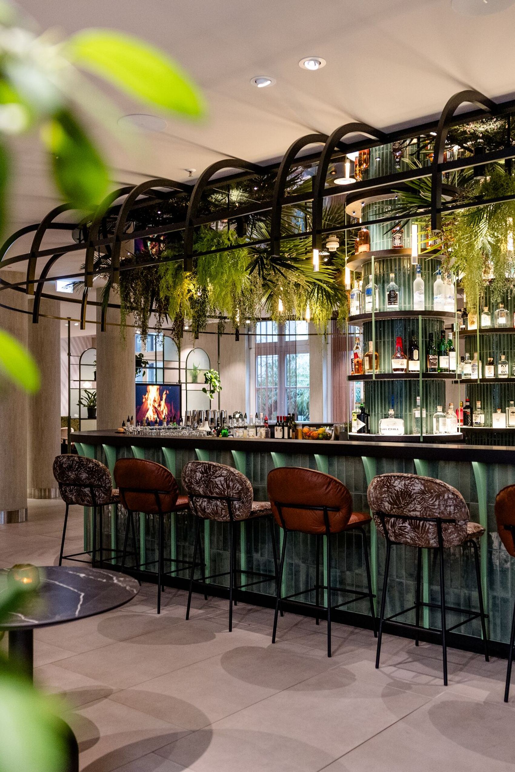 Designhotel Frankfurt-Hauptbahnhof Motel One Bar mit Barhockern, grüner Pflanzen-Dekoration und stilvoll angeordneten Getränkeflaschen.