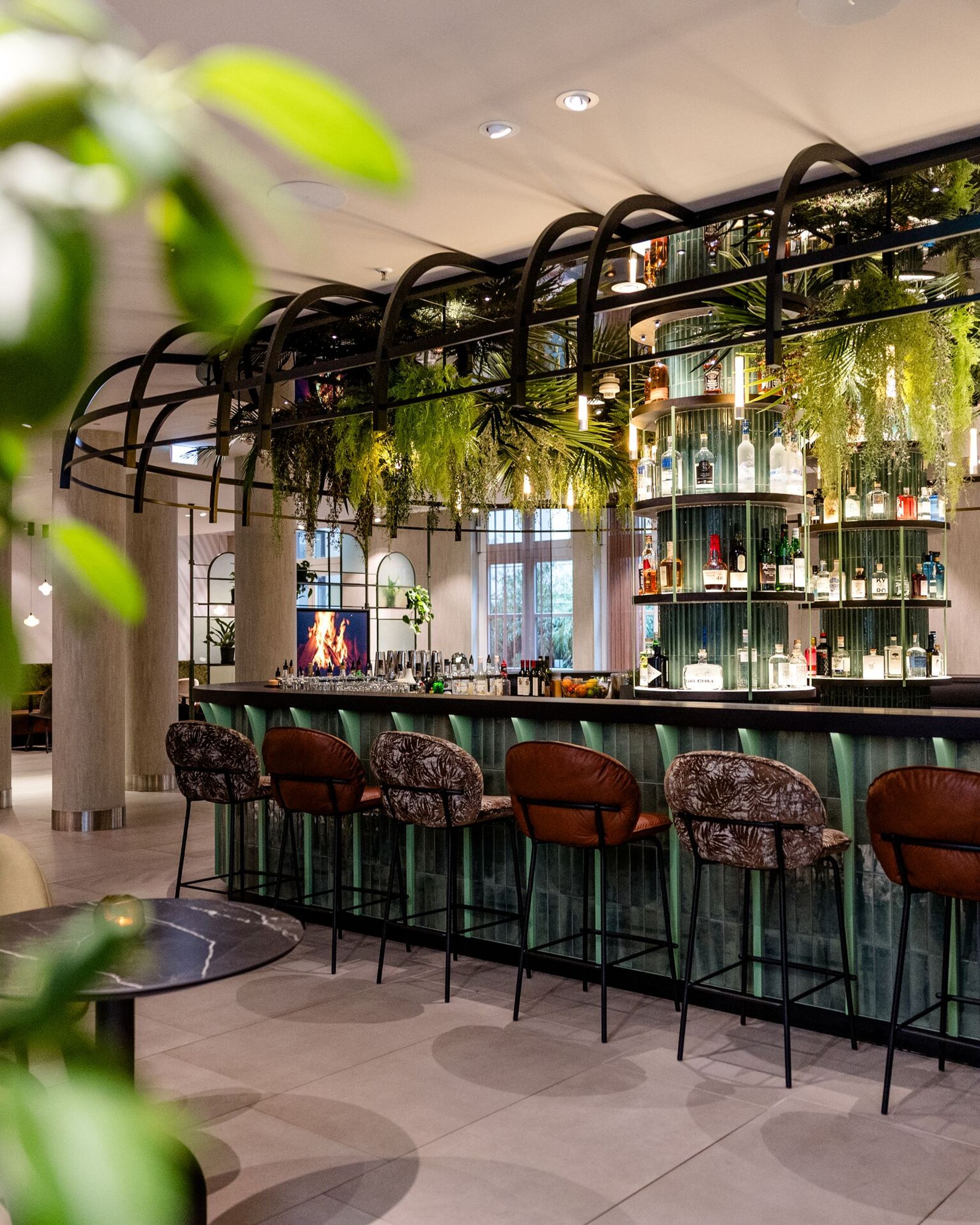 Designhotel Frankfurt-Hauptbahnhof Motel One Bar mit Barhockern, grüner Pflanzen-Dekoration und stilvoll angeordneten Getränkeflaschen.
