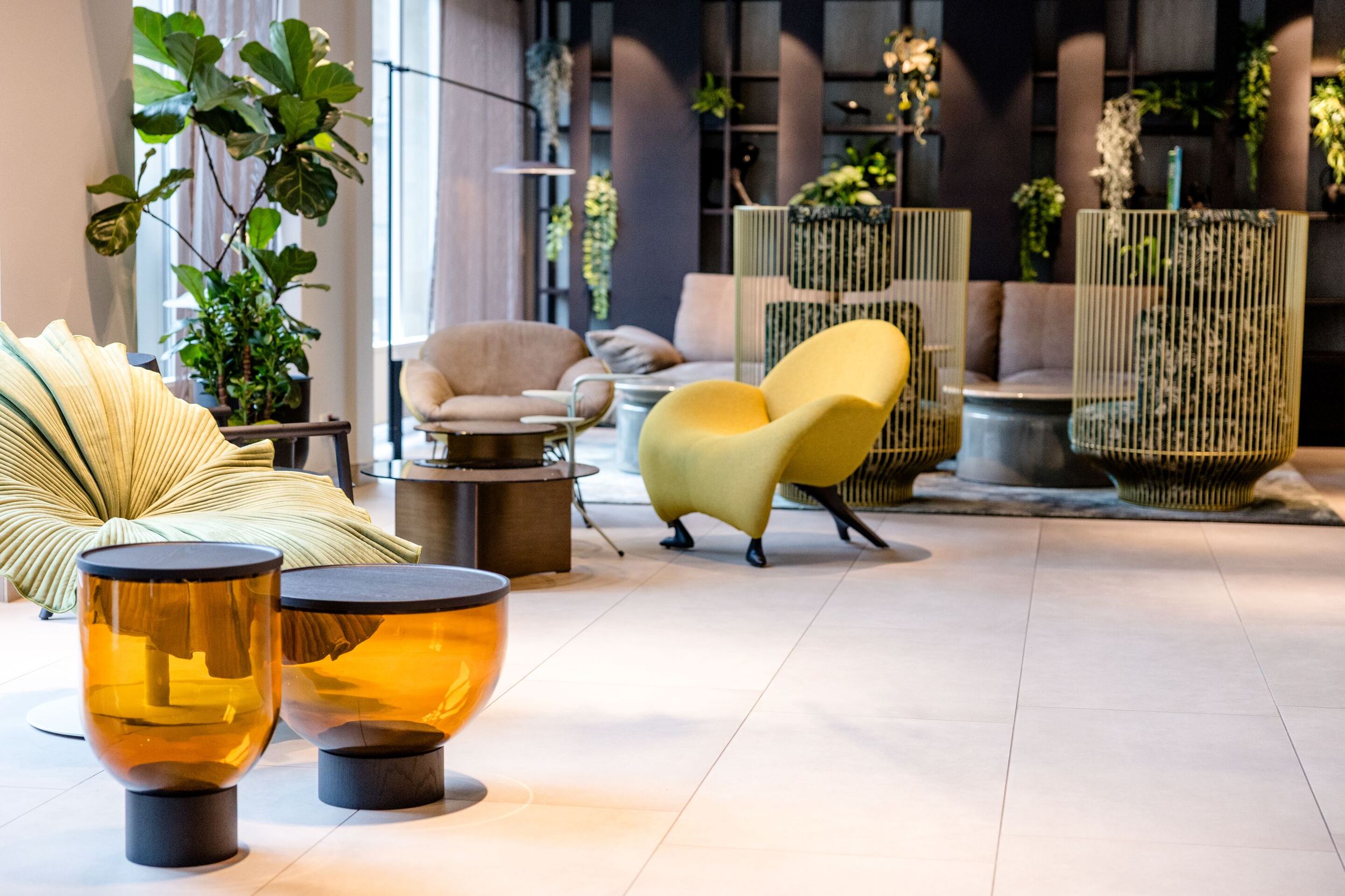 Designhotel Frankfurt-Hauptbahnhof Motel One Lounge mit modernen Sesseln, bequemen Sofas und orangen Beistelltischen. Grüne Pflanzen und dezente Beleuchtung.