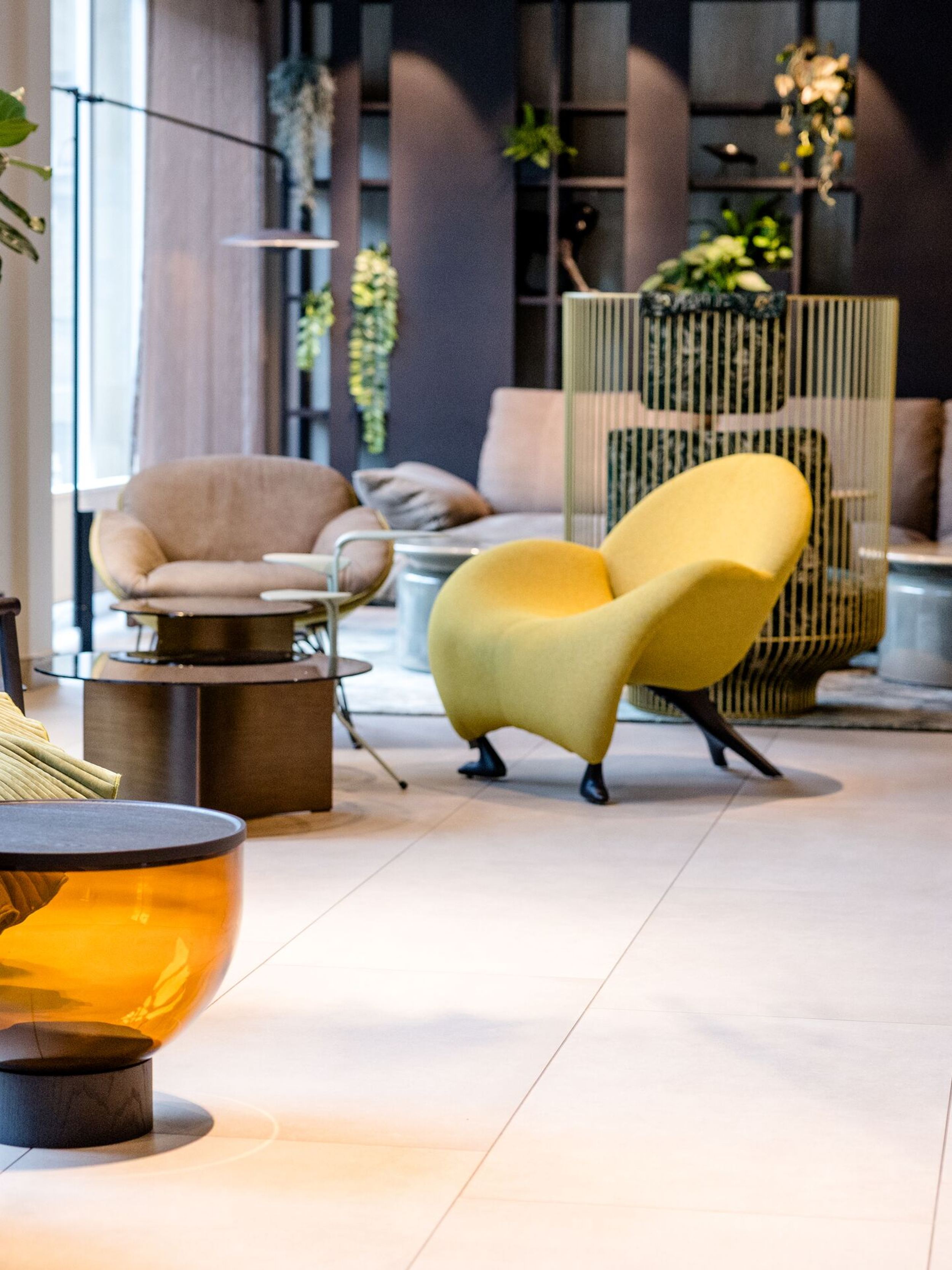 Designhotel Frankfurt-Hauptbahnhof Motel One Lounge mit modernen Sesseln, bequemen Sofas und orangen Beistelltischen. Grüne Pflanzen und dezente Beleuchtung.