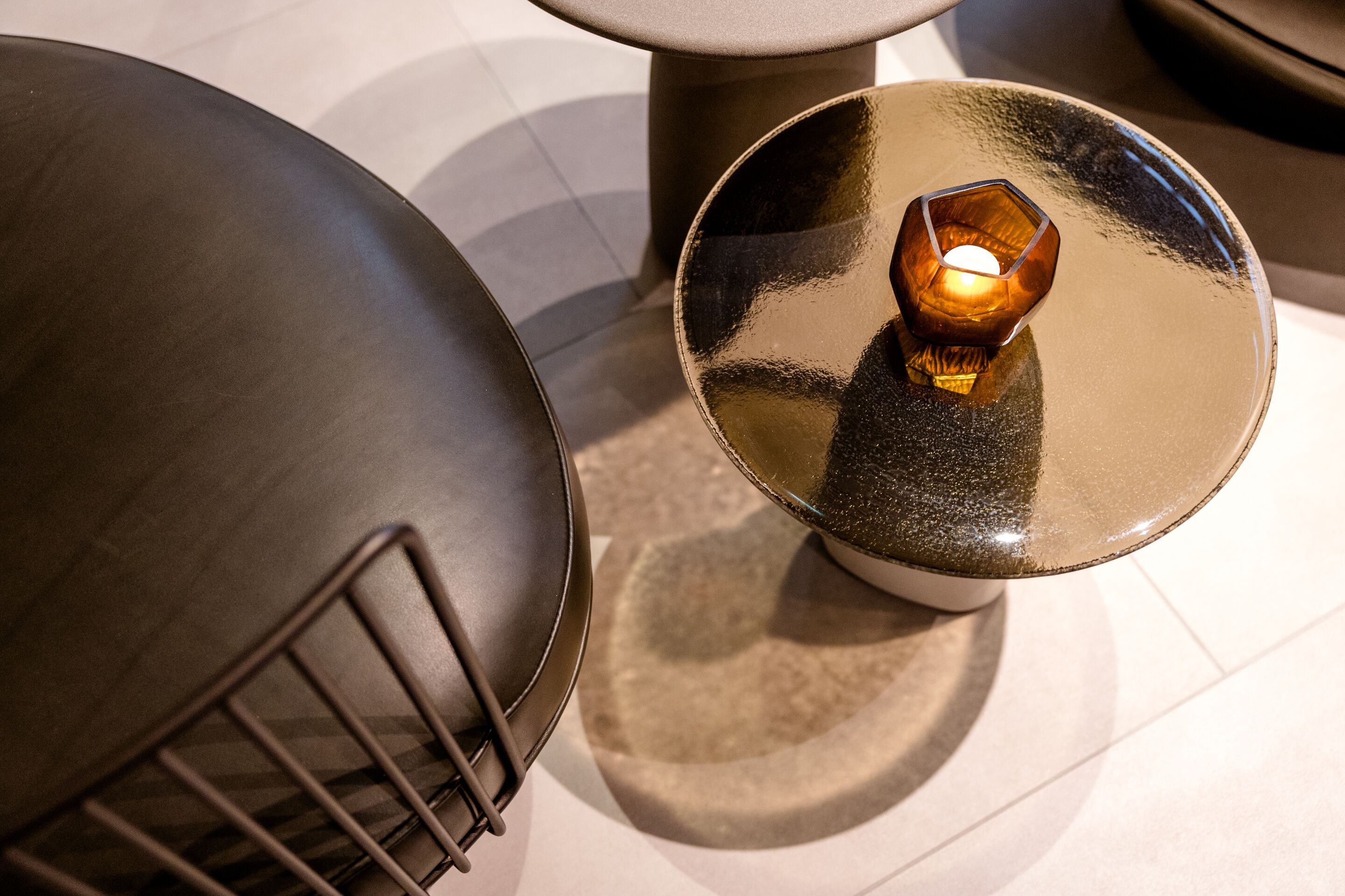 Hotel Frankfurt-Hauptbahnhof Motel One Blick von oben auf einen Beistelltisch mit glänzender Oberfläche und brennender Kerze, daneben ein schwarzer Stuhl mit Metallgestell.