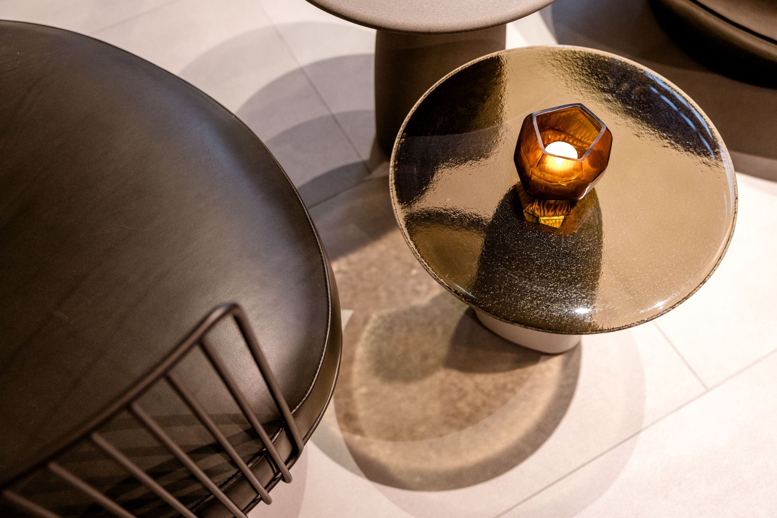Hotel Frankfurt-Hauptbahnhof Motel One Blick von oben auf einen Beistelltisch mit glänzender Oberfläche und brennender Kerze, daneben ein schwarzer Stuhl mit Metallgestell.