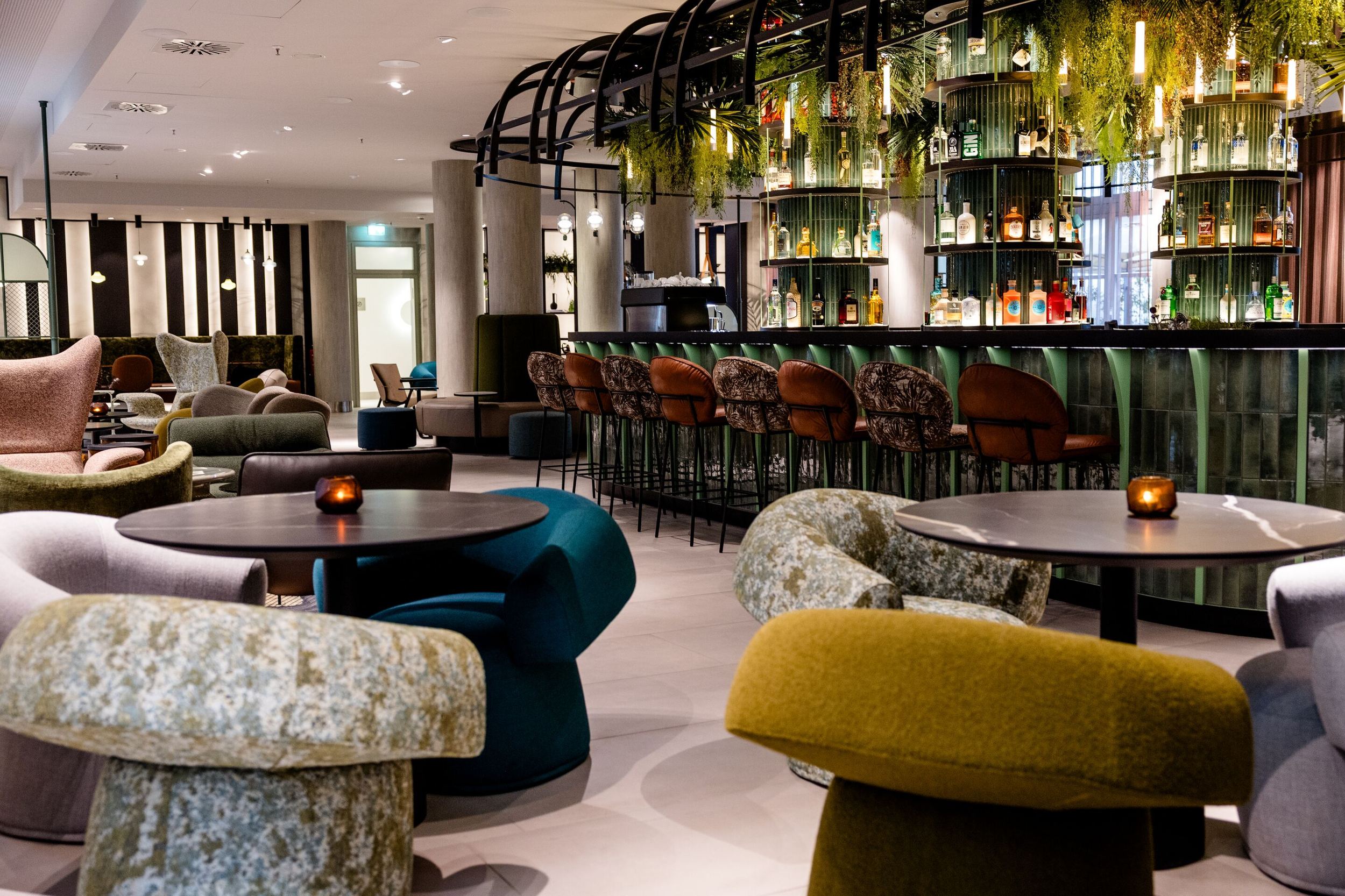 Designhotel Frankfurt-Hauptbahnhof Motel One Bar mit mehreren Sitzgelegenheiten, warmem Licht und grün dekoriertem Tresen.
