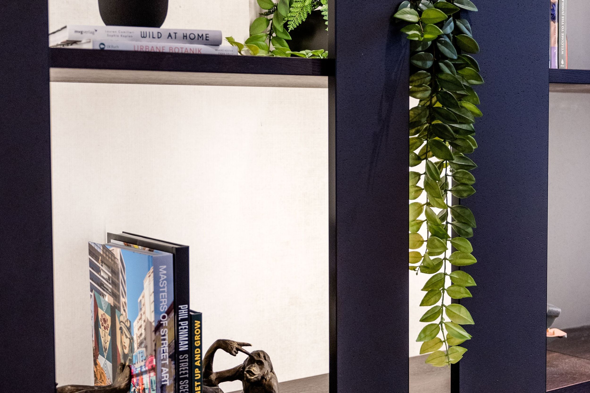 Designhotel Frankfurt-Hauptbahnhof Motel One Wandregal mit Dekorationen wie eine schwarze Vase, Bücher, eine Skulptur sowie grüne Pflanzen.