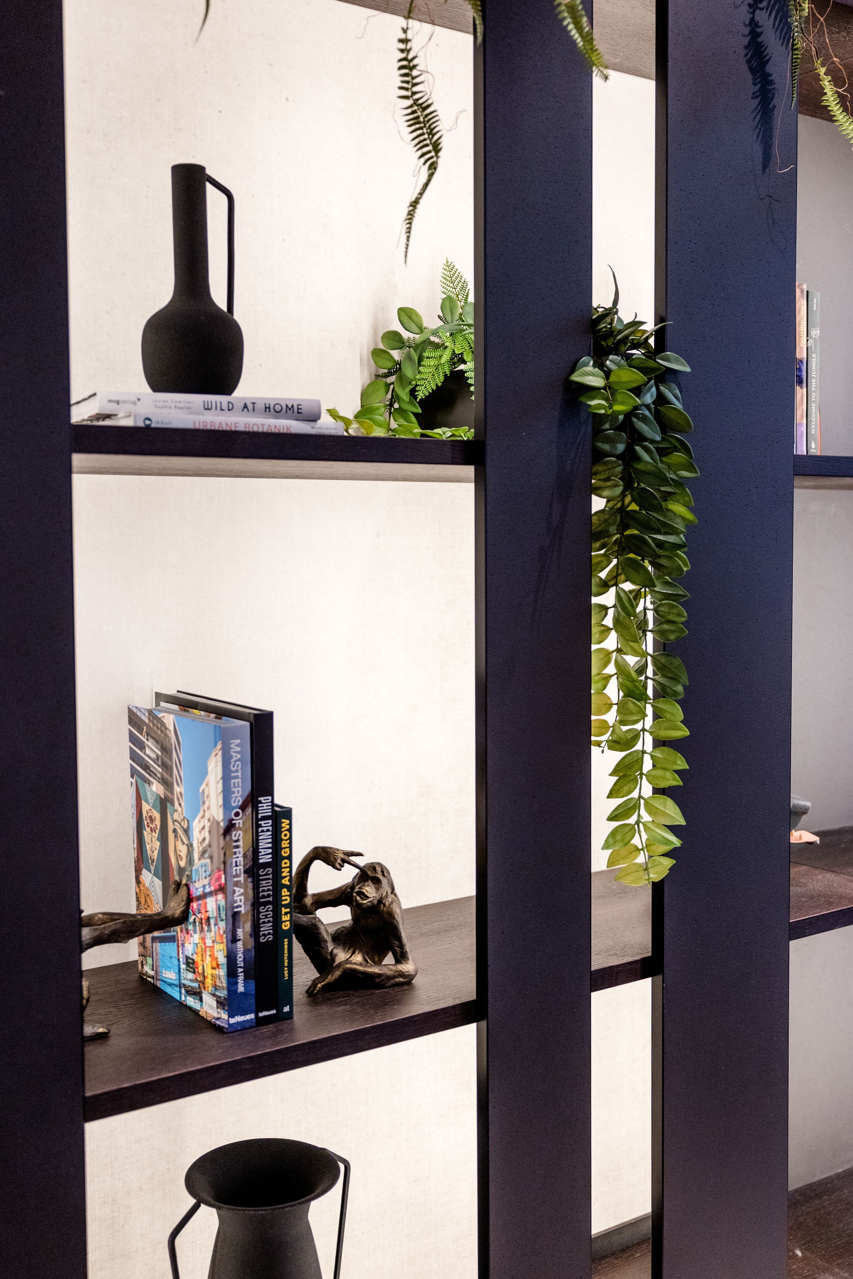 Designhotel Frankfurt-Hauptbahnhof Motel One Wandregal mit Dekorationen wie eine schwarze Vase, Bücher, eine Skulptur sowie grüne Pflanzen. Designhotel Frankfurt-Hauptbahnhof Motel One Wandregal mit Dekorationen wie eine schwarze Vase, Bücher, eine Skulptur sowie grüne Pflanzen.