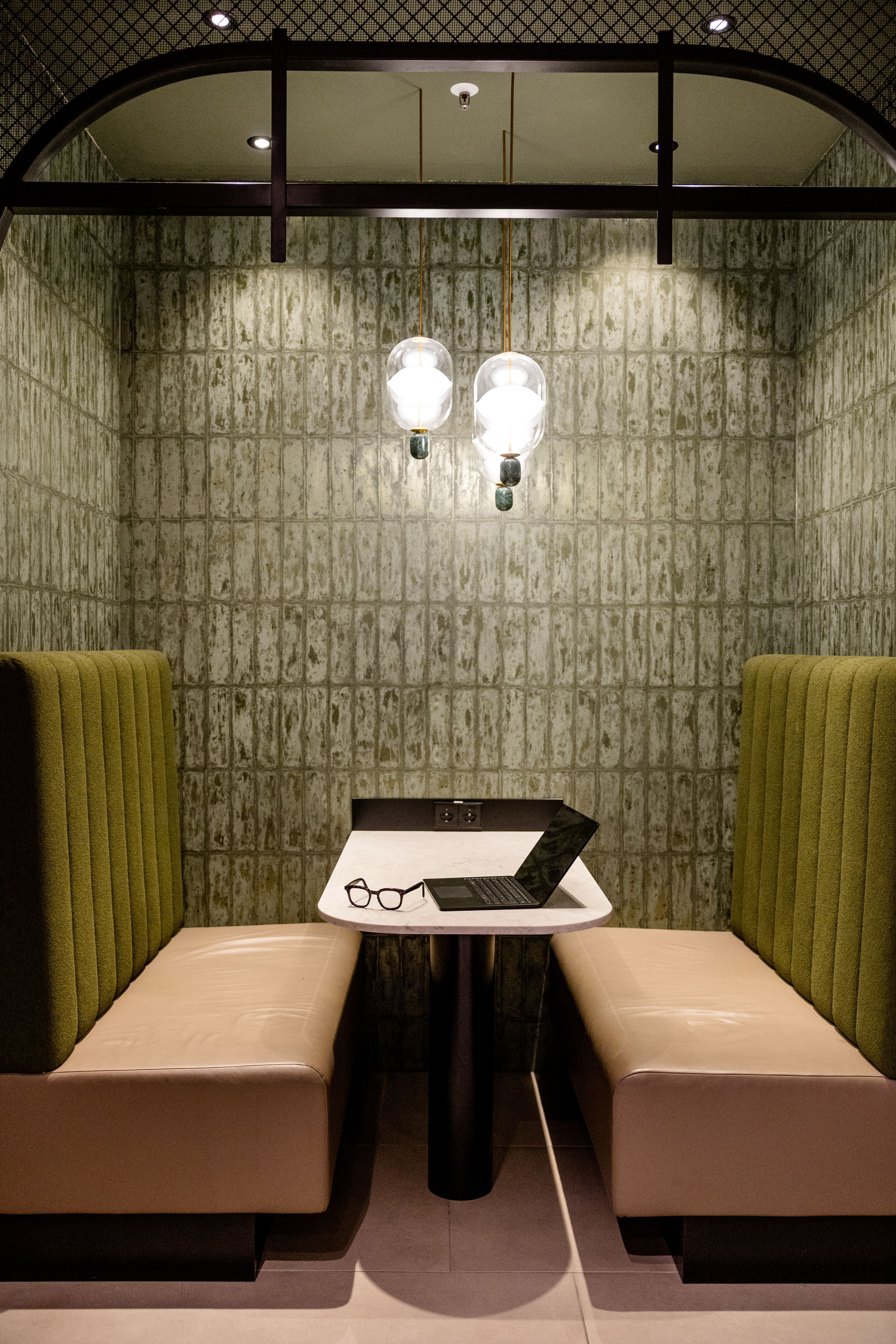 Hotel Frankfurt-Hauptbahnhof Motel One Sitzecke mit zwei gepolsterten Bänken und einem Tisch, beleuchtet von zwei Wandlampen. Ein Laptop und eine Brille liegen auf dem Tisch.