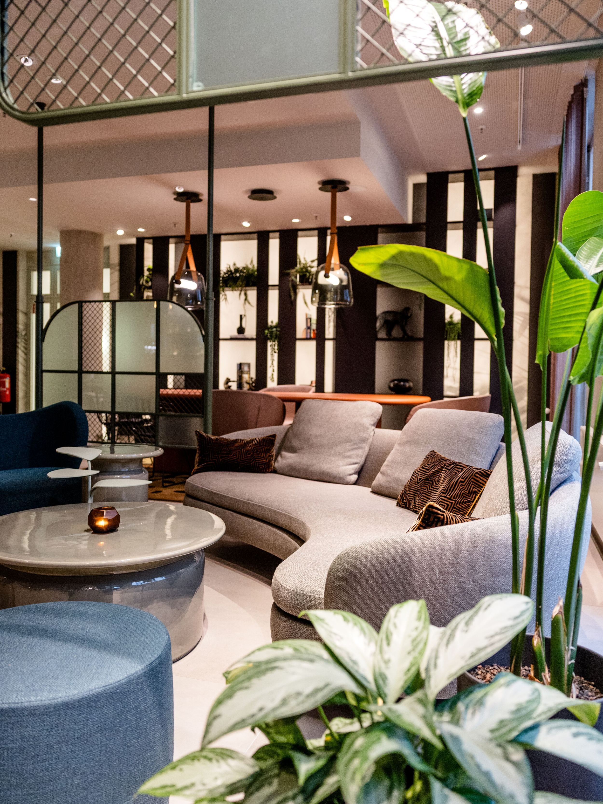 Hotel Frankfurt-Hauptbahnhof Motel One gemütliche Lounge mit geschwungenem Sofa, warmen Lichtakzenten und grünen Pflanzen schafft eine Atmosphäre zum Entspannen und Verweilen.