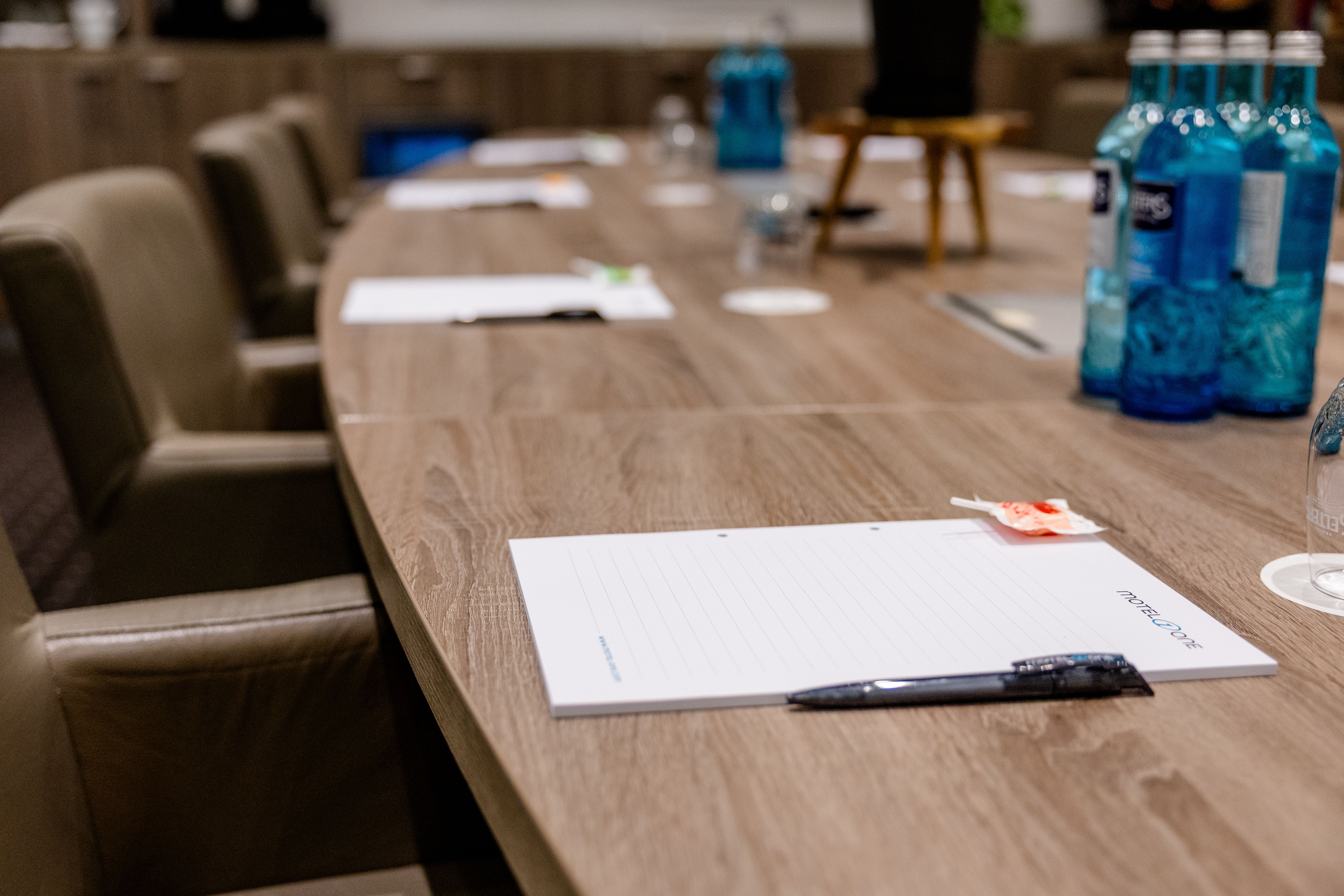 Konferenzraum mit ovalem Holztisch, bequemen Stühlen, Notizblöcken, Stiften und Wasserflaschen, bereit für eine Besprechung oder ein Meeting.
