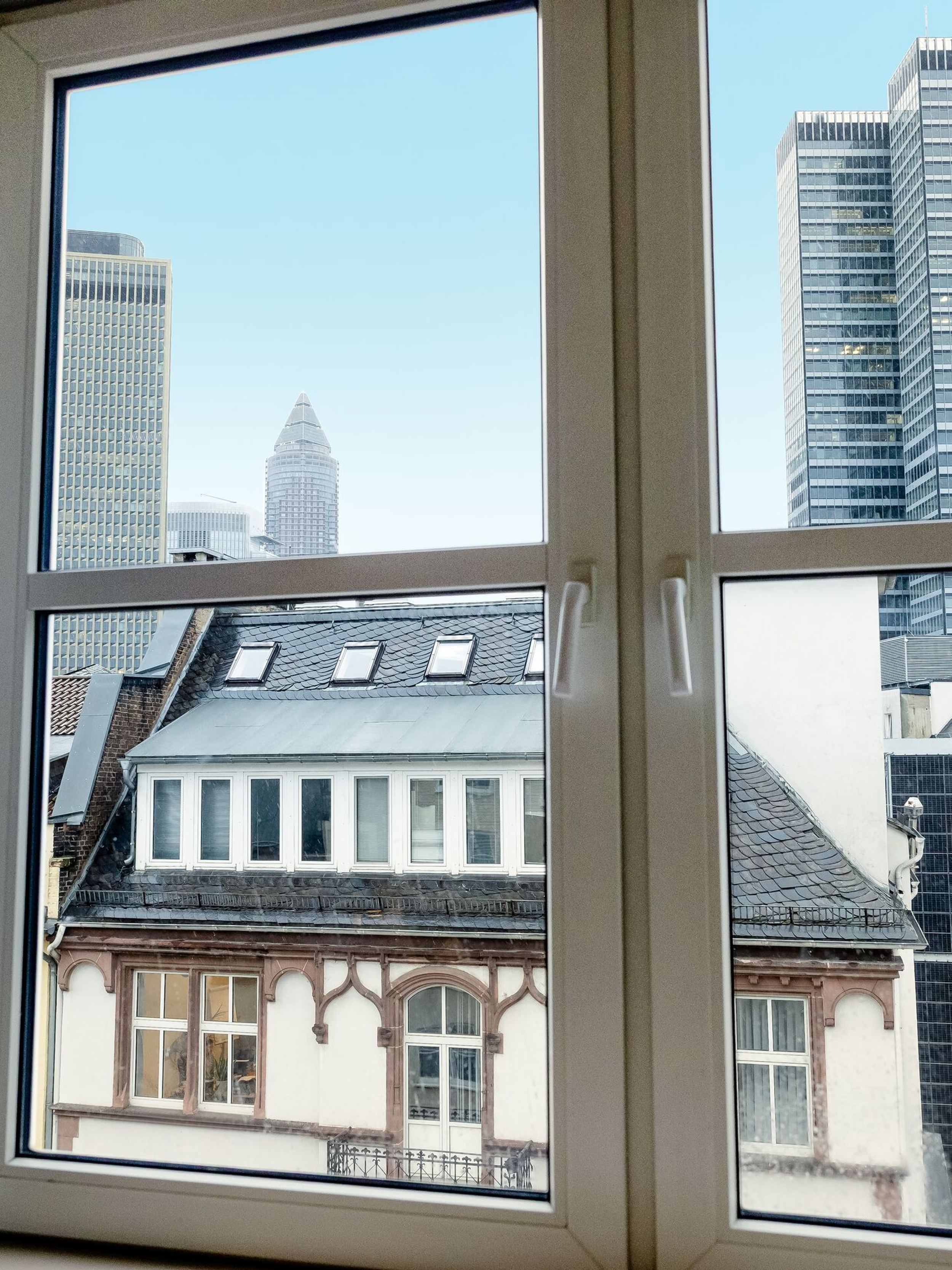 Hotel Frankfurt Hauptbahnhof Motel One Blick aus dem Hotelzimmerfenster auf die Frankfurter Skyline mit modernen Hochhäusern und historischen Gebäuden, bei klarem Himmel.