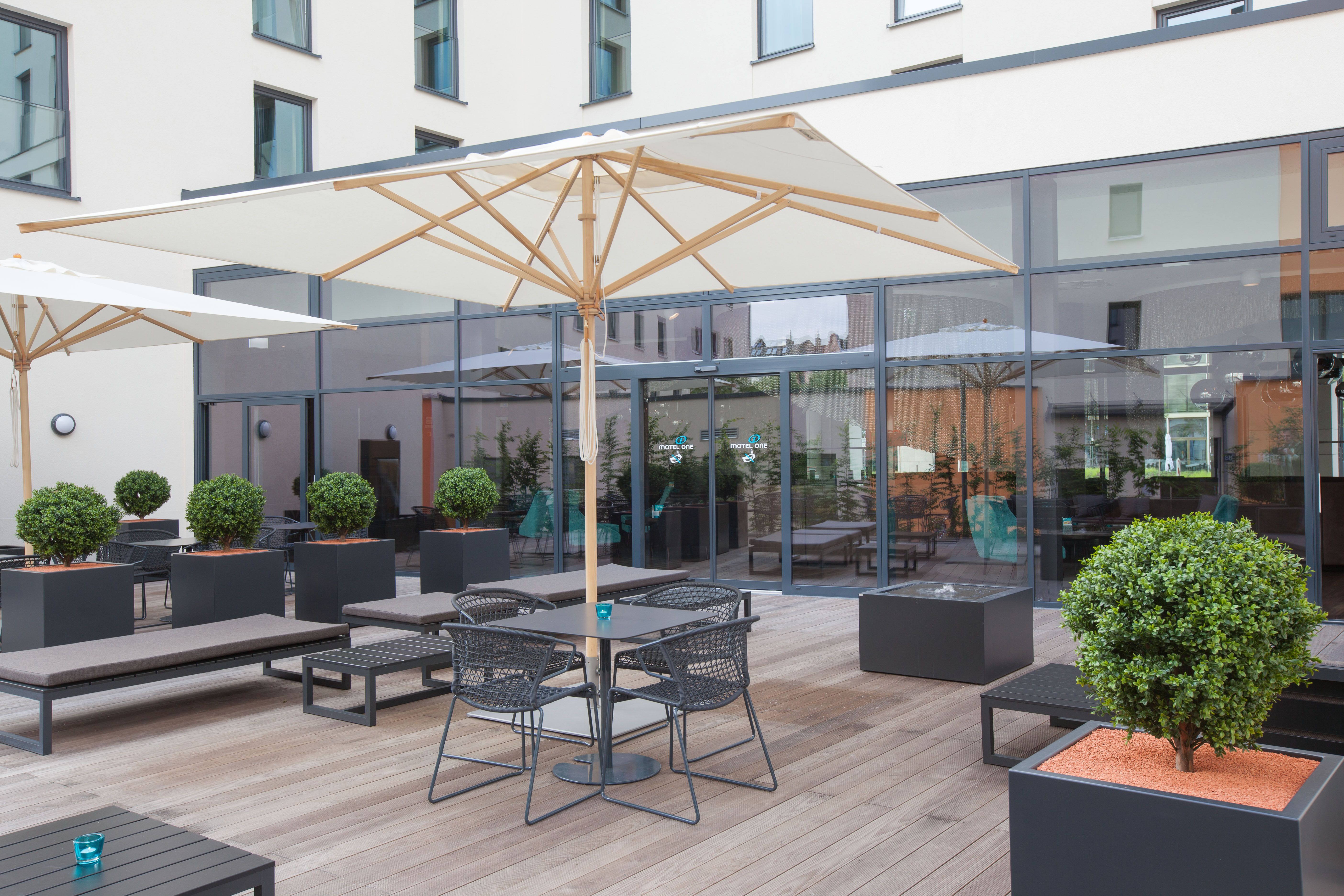 Hotel Frankfurt Messe Motel One Außenbereich mit Sitzgelegenheiten, Sonnenschirm und Eingangstür