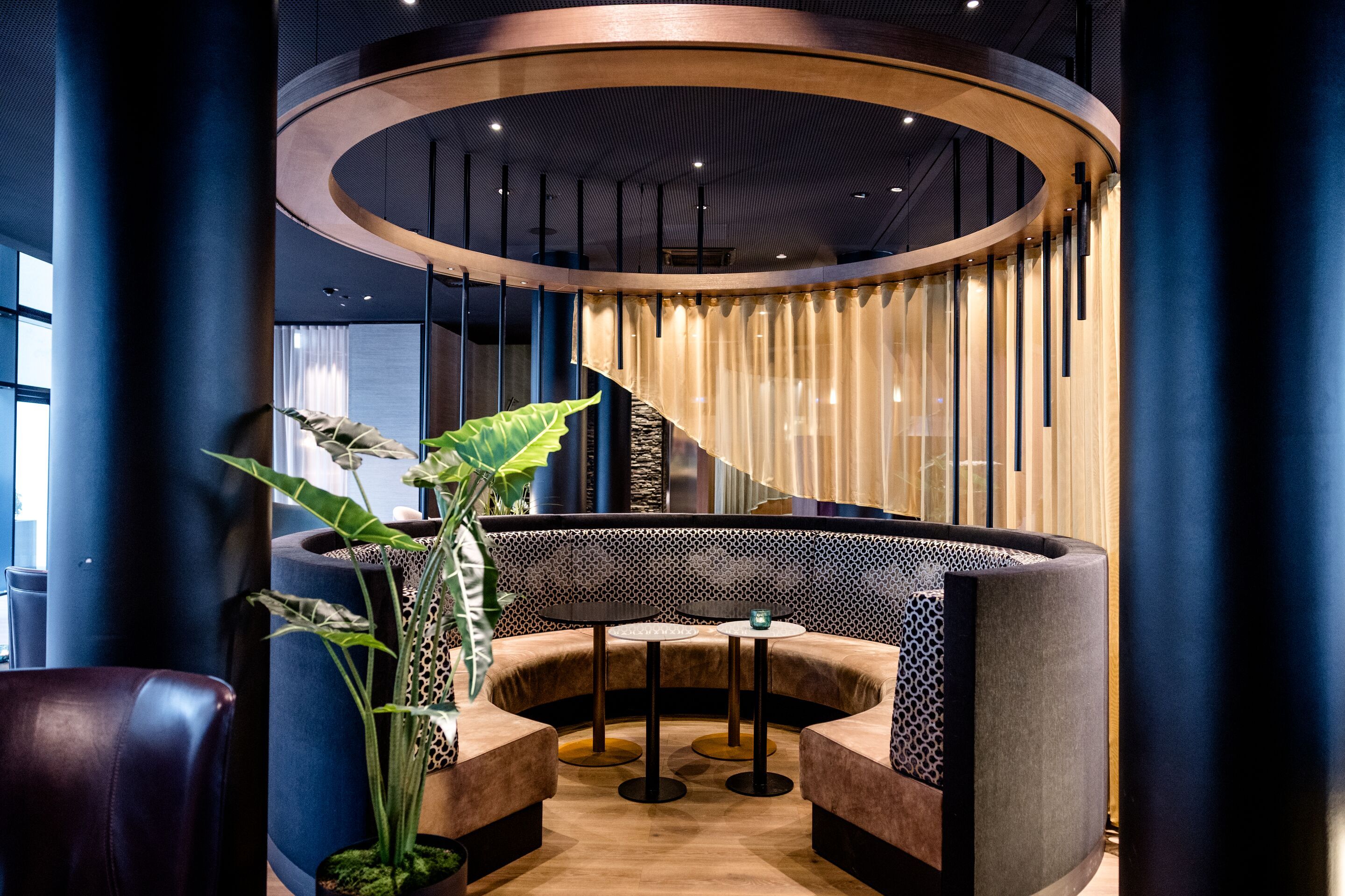 Hotel Frankfurt-Messe Motel One gemütliche, halbrunde Sitznische mit gepolsterten Bänken, modernem Deckenring und Holzvertäfelung, umgeben von stilvoller, eleganter Atmosphäre für entspannte Gespräche oder Arbeit.