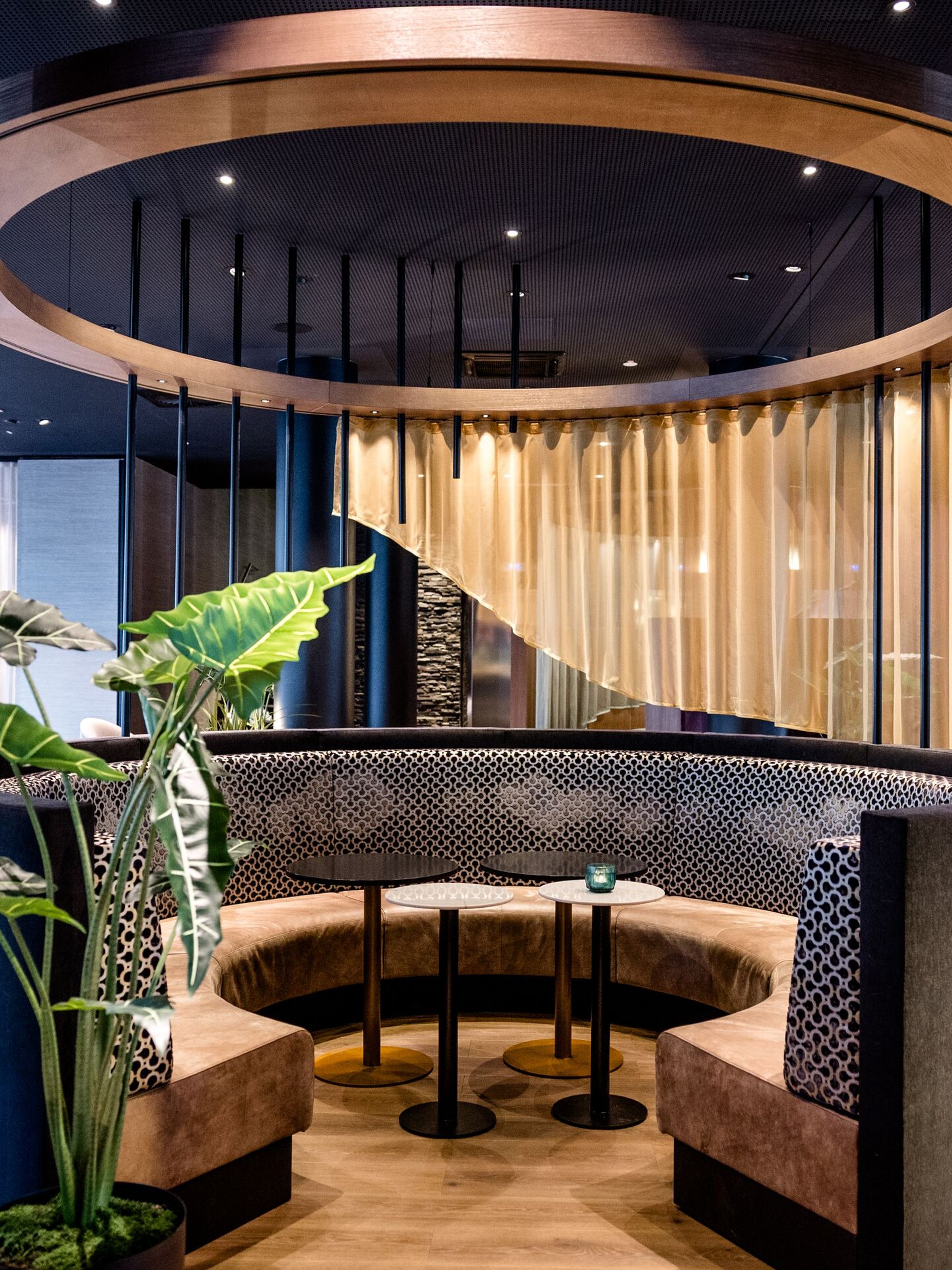 Hotel Frankfurt-Messe Motel One gemütliche, halbrunde Sitznische mit gepolsterten Bänken, modernem Deckenring und Holzvertäfelung, umgeben von stilvoller, eleganter Atmosphäre für entspannte Gespräche oder Arbeit.