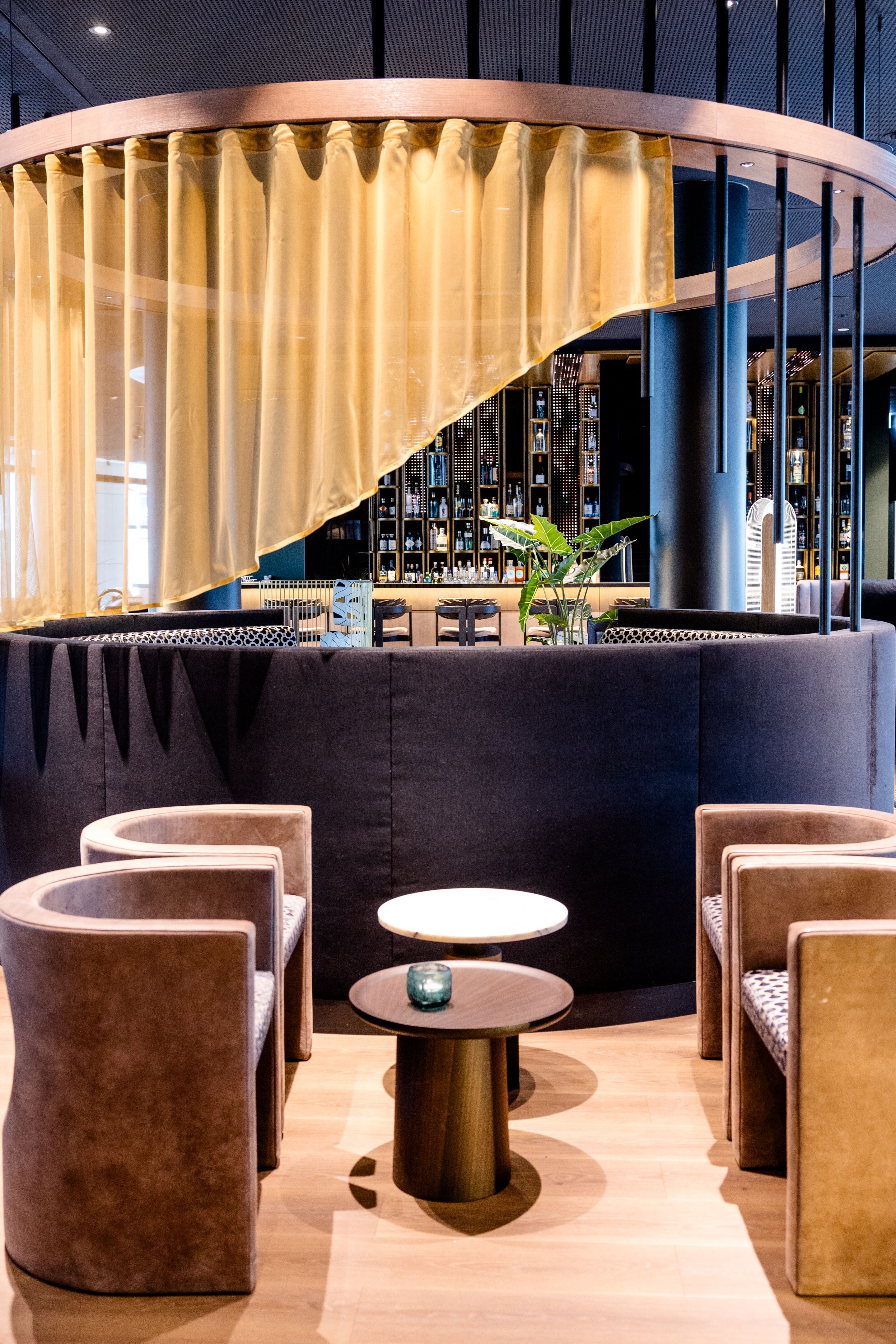 Hotel Frankfurt-Messe Motel One Loungbereich mit Sesseln und kleinen Tischen, abgetrennt durch einen halbtransparenten Vorhang, warmes, modernes Ambiente ideal zum Entspannen oder geselligen Beisammensein.