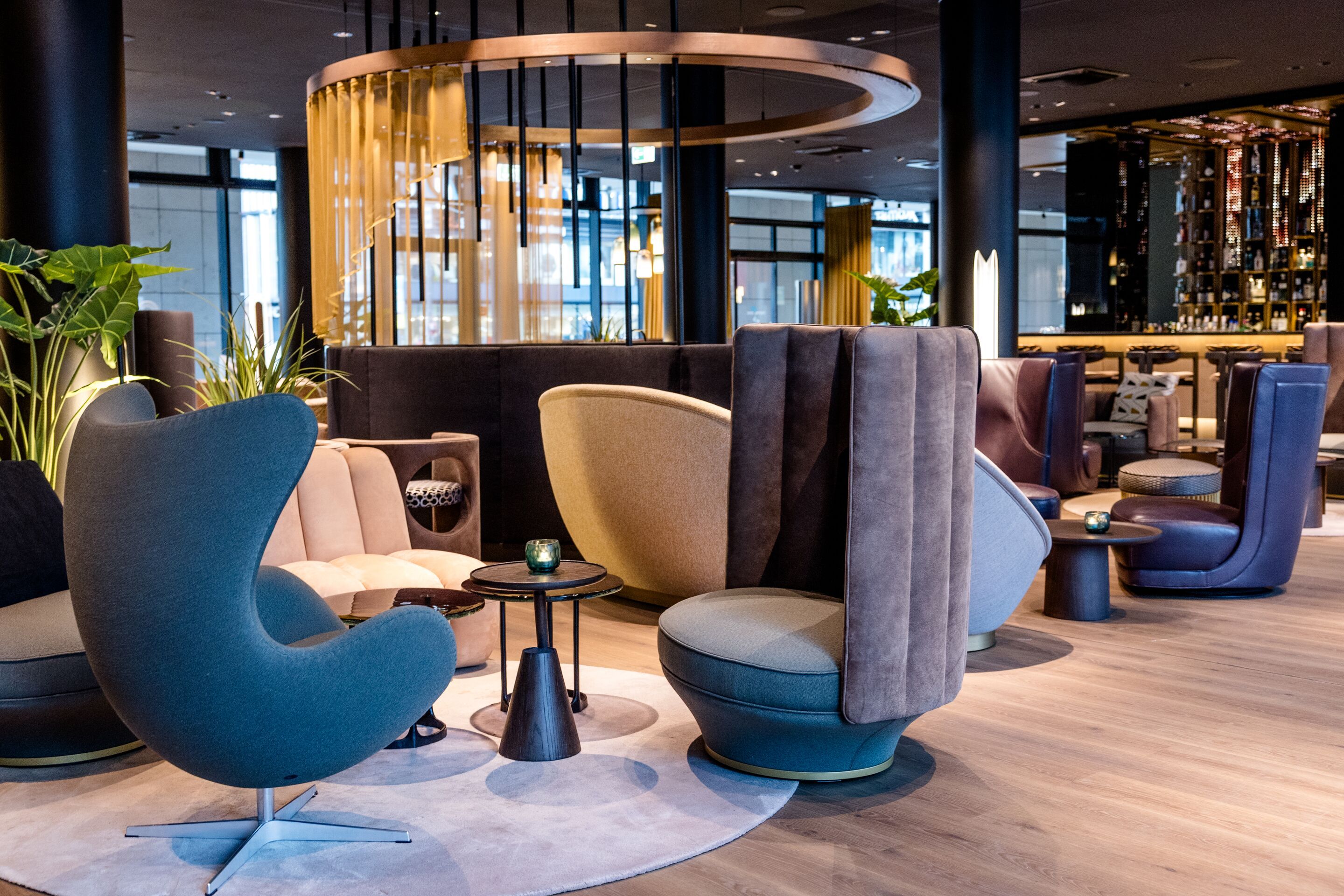 Hotel Frankfurt-Messe Motel One Lounge mit stilvollen, farblich abgestimmten Sesseln und großen Fenstern, die ein entspanntes Ambiente schaffen. Dezente Beleuchtung und edle Holzelemente unterstreichen das einladende Design.