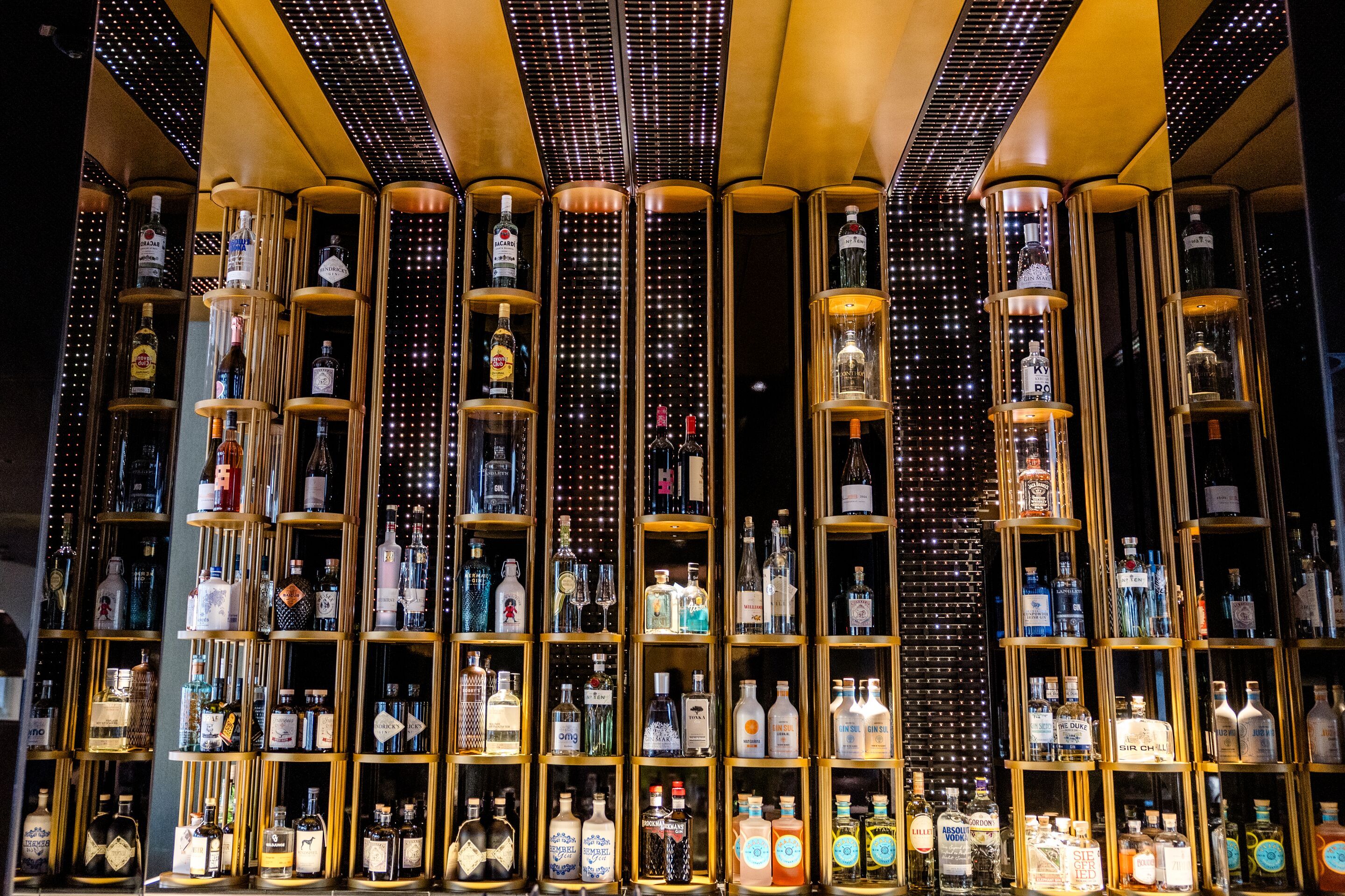 Hotel Frankfurt-Messe Motel One Bar mit beleuchteten Regalen, die eine vielfältige Auswahl an Spirituosen und edlen Getränken präsentieren.