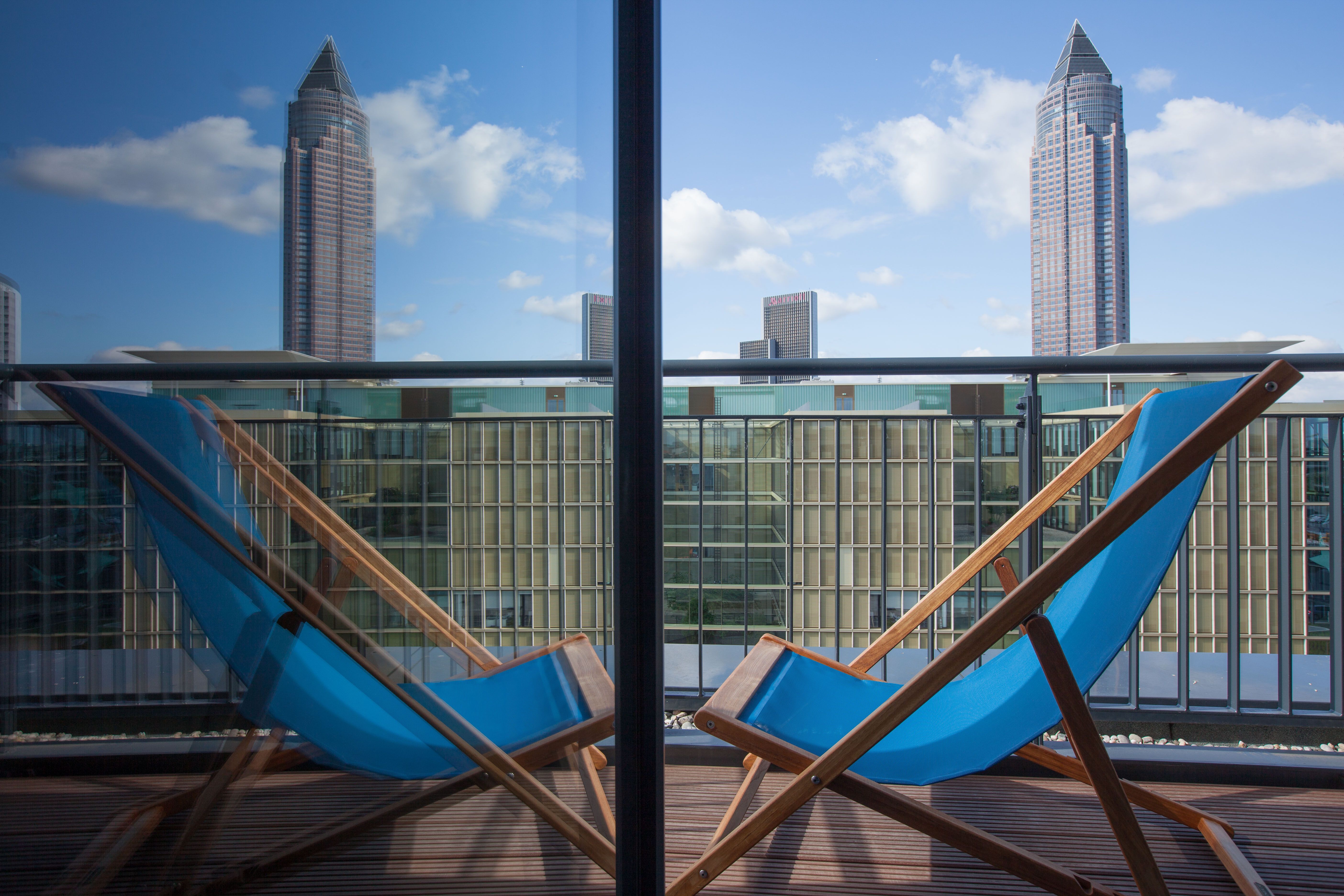 Hotel Frankfurt Messe Motel One Balkonzimmer mit Liegestuhl und Aussicht auf die Hochhäuser der Stadt