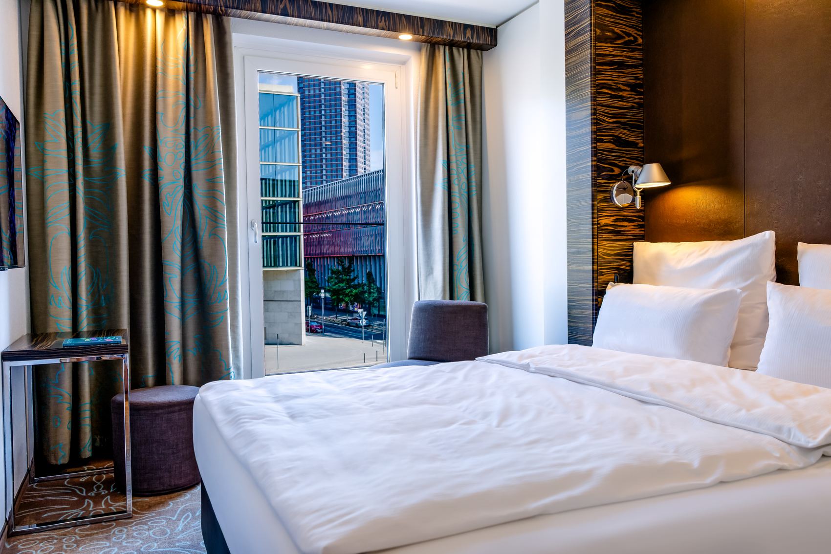 Gemütliches Hotelzimmer mit großem Bett, weicher Beleuchtung und Zugang zu einem Balkon mit Stadtblick, ideal für erholsamen Aufenthalt in urbaner Umgebung.