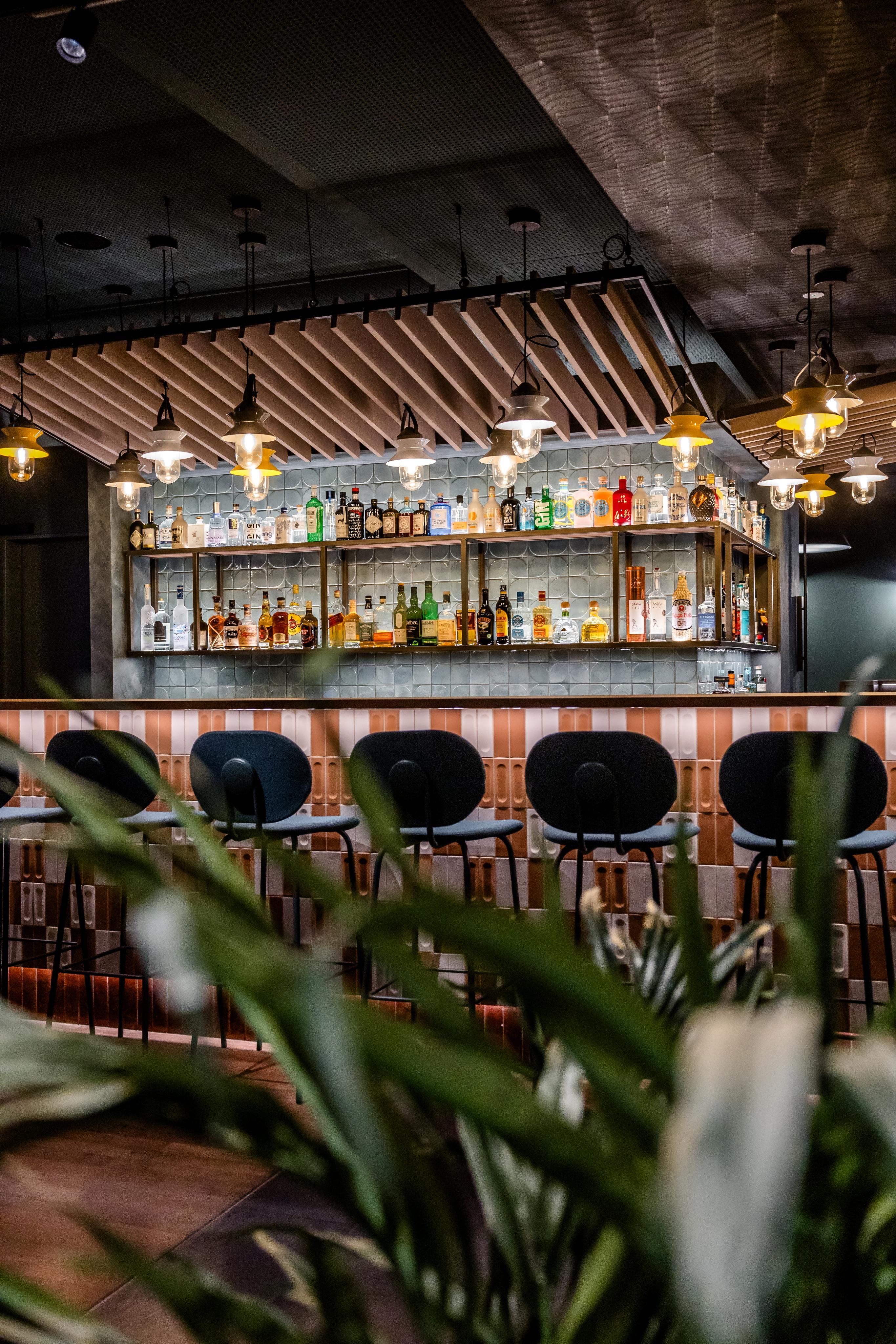Moderne Hotelbar mit stilvoller Beleuchtung, einer Auswahl an Spirituosen hinter der Theke und eleganten Barhockern, umgeben von warmem, einladendem Ambiente.