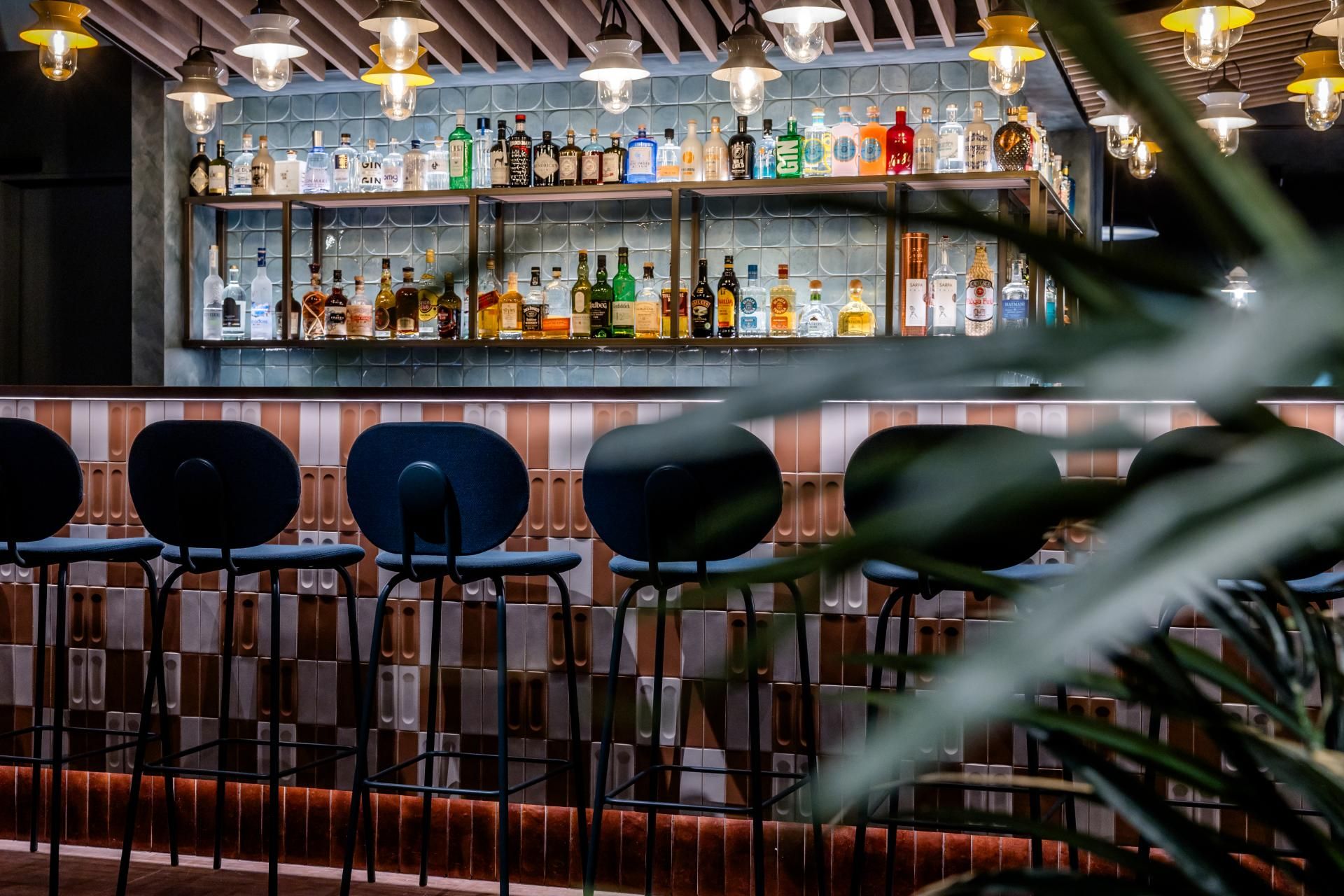 Moderne Hotelbar mit hoher Theke, schwarzen Barhockern und einer großen Auswahl an Getränken auf beleuchteten Regalen, umgeben von stilvoller Beleuchtung und gemütlicher Atmosphäre.